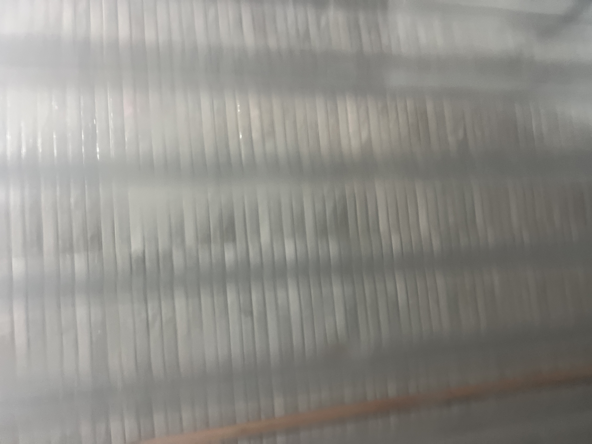 A blurry, abstract image shows a light-colored, textured surface with horizontal lines. A vertical, reddish-brown object is visible on the left side of the frame, extending from top to bottom. The overall impression is of a translucent or frosted material with subtle variations in light and shadow creating a layered effect. The image does not depict any identifiable features of Casablanca, Morocco.