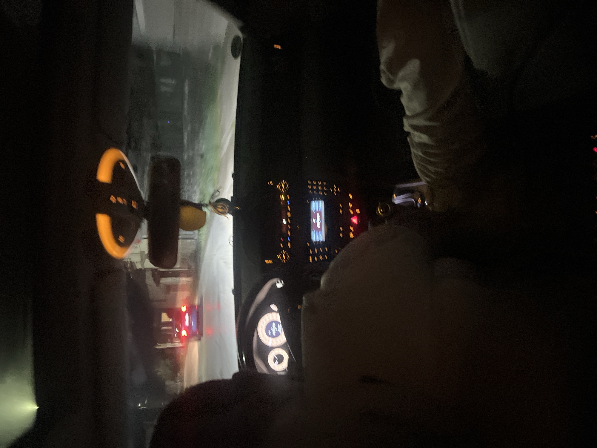 The image shows the interior of a car at night. The dashboard and steering wheel are visible, as well as the driver and front passenger, partially obscured by darkness. The exterior view through the windshield shows a road illuminated by headlights, with buildings and other vehicles. There is no information in the photo to locate the place in Gorna Rositsa, Bulgaria.
