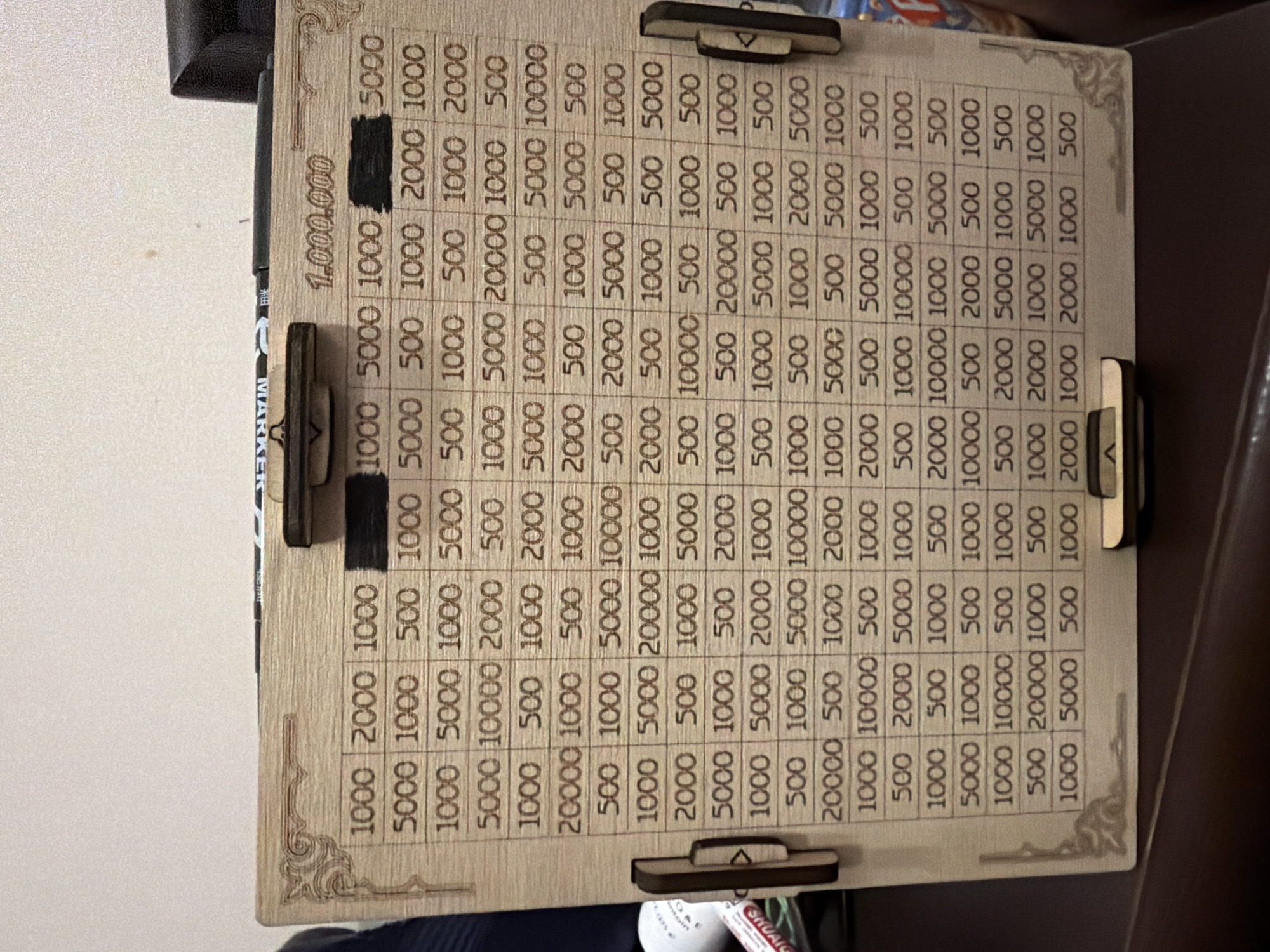 The image shows a wooden board with a grid of numbers. The numbers range from 500 to 20,000, with a title at the top reading "1,000,000." There are slider markers positioned around the edges of the board, used to mark progress or scores. The board is likely used for a game or for tracking savings goals.
There is no indication of the location being Yerevan, Armenia, or any specific city. The description focuses solely on the elements visible in the image.