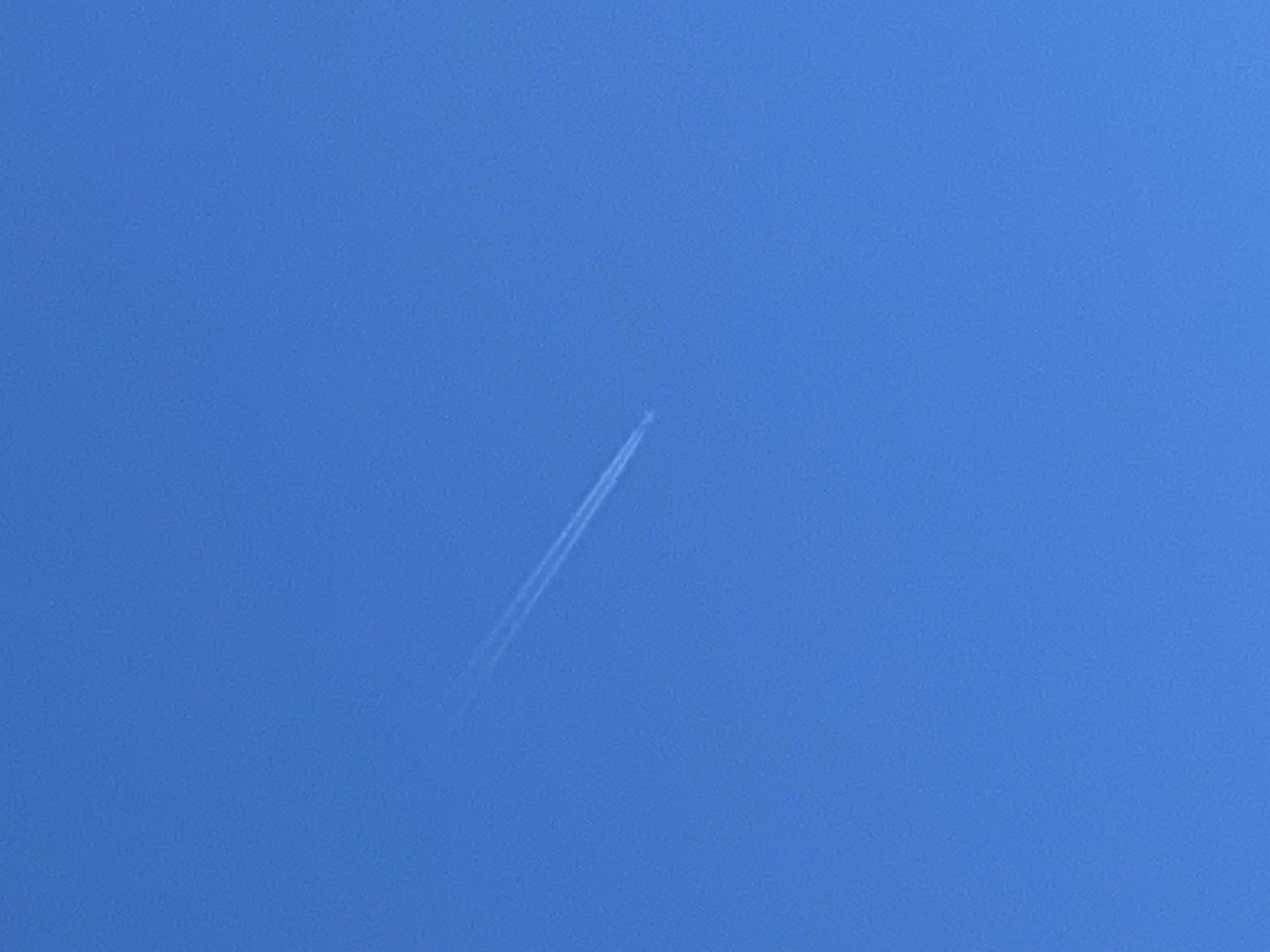 A vapor trail from an airplane is visible against a clear blue sky. The trail is white and appears as a straight line going from the bottom to the top of the image. The absence of other objects suggests the scene is taken from a wide open area. No people are visible. The city name Гаревая, Russia is irrelevant as the sky is visible from anywhere.