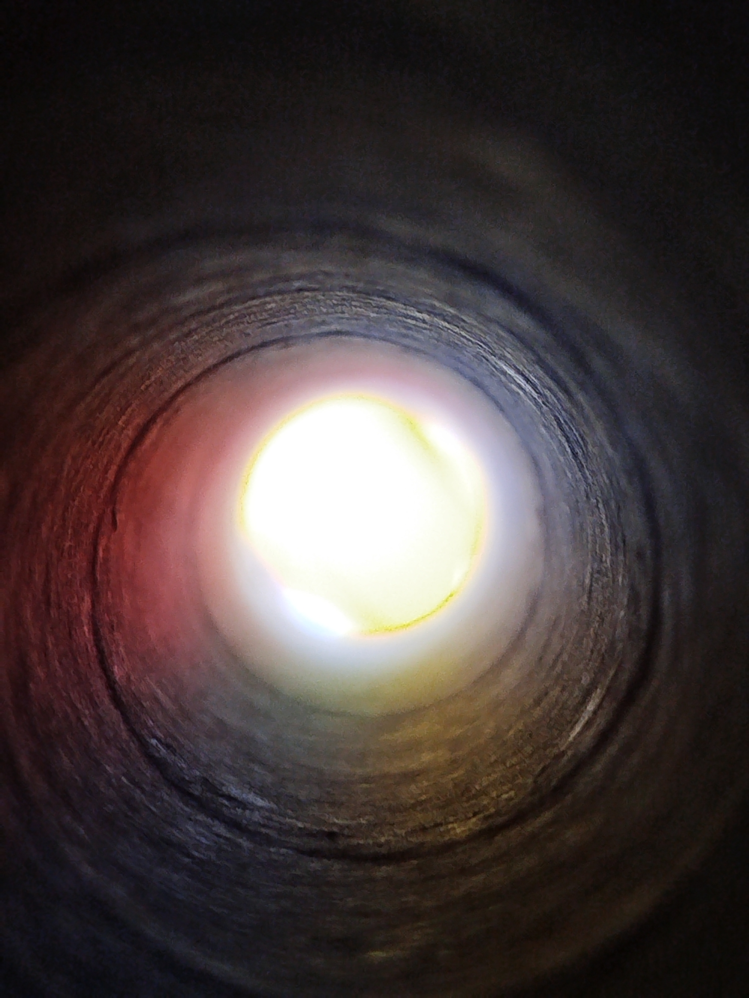 The image shows a view looking down a dark, cylindrical tunnel with a bright light at the end. The tunnel walls appear rough and textured, with swirling patterns. There are reddish and yellowish hues present on the walls near the light source. The overall impression is one of looking into a deep, artificial void. The location in Kremenchuk, Ukraine, is not discernable from the image itself, as it depicts an abstract, internal perspective devoid of any identifying landmarks or context.