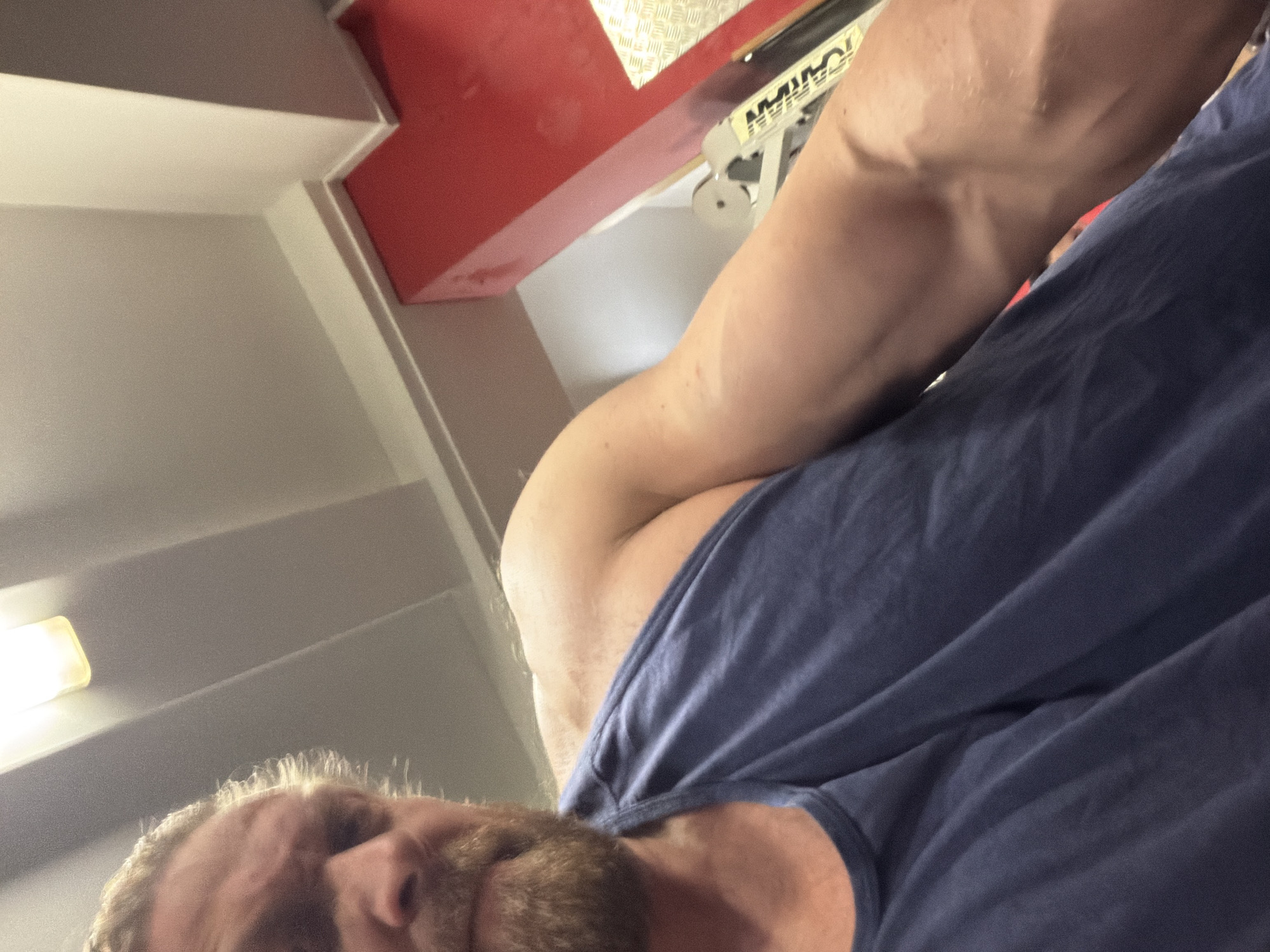 A low-angle shot depicts a person with fair skin and a beard, wearing a blue t-shirt. The person's right arm, noticeably muscular with visible veins, is angled toward the camera. The background includes a ceiling with recessed lighting and a piece of red and white equipment. The city of Saint Petersburg, Russia, cannot be determined from the provided information.