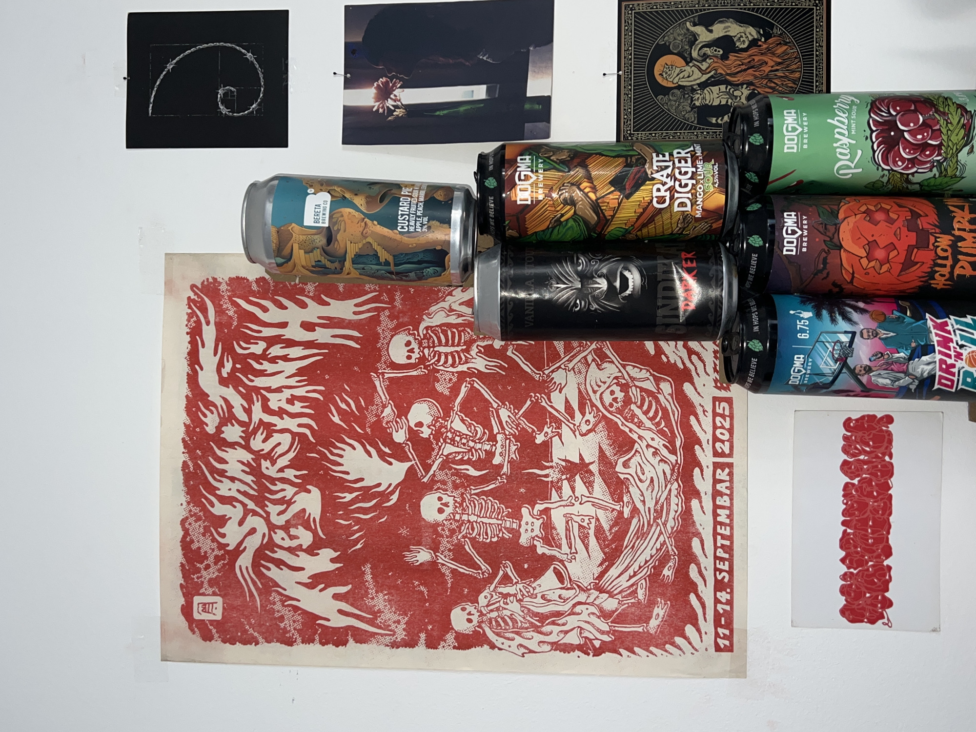 The image presents a collection of items affixed to a white wall. At the top left, there is a black square depicting a spiral. To its right is a photograph of a person holding a flower. Further right is an image printed in black and gold.
Below these are a series of beer cans. From left to right, their labels read "BERETA Brewing Co Custard Pie," "DOGMA Brewery Crate Digger," "DOGMA Brewery Raspberry," "SINDICRATE DARKER," and "DOGMA Brewery Hollow Pumpkin,".
To the lower left is a red and white poster featuring a skeletal design and the text "11-14. SEPTEMBAR 2025". Below this, another poster is displayed, featuring red marks.
There is no information available to confidently pinpoint the location in Belgrade, Serbia, or to detail any specific actions or interactions within the scene.