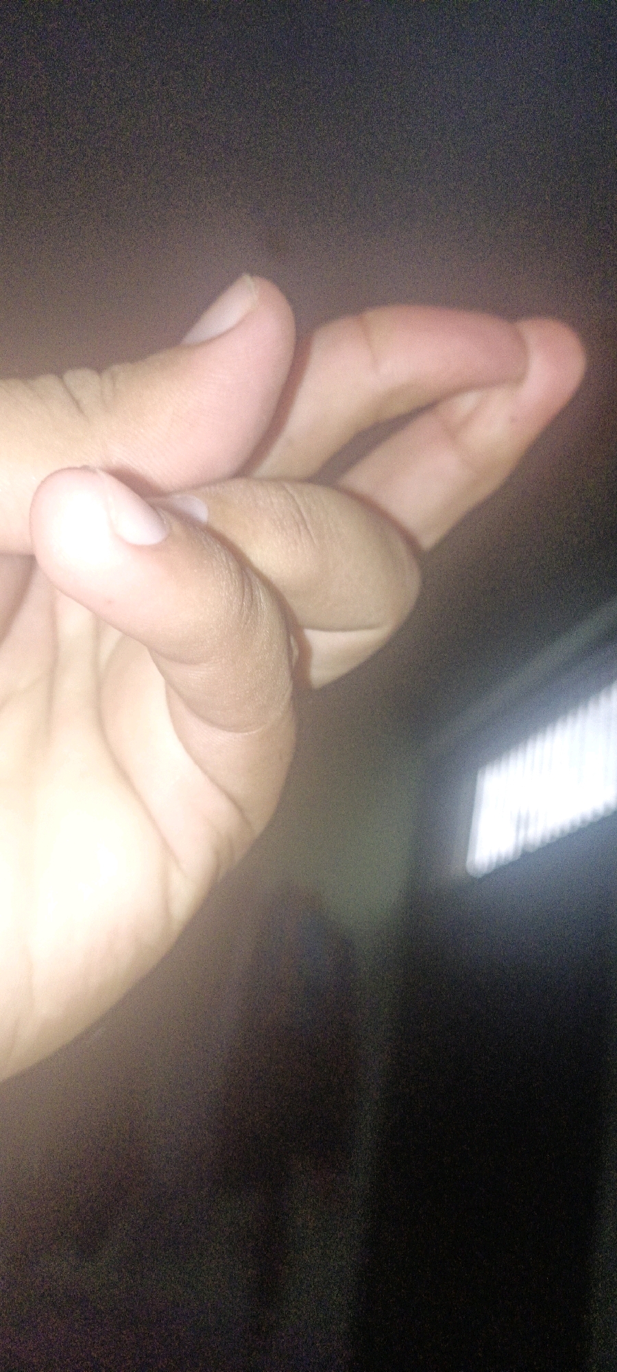 The image shows a close-up of a person's hand, with the thumb and index finger forming a pinch-like gesture. The hand is positioned in the foreground, and the background is dark and out of focus, with a bright, horizontal stripe of light visible on the right side. There is no visible indication of the location being CHAK NO.172 TDA, Pakistan.