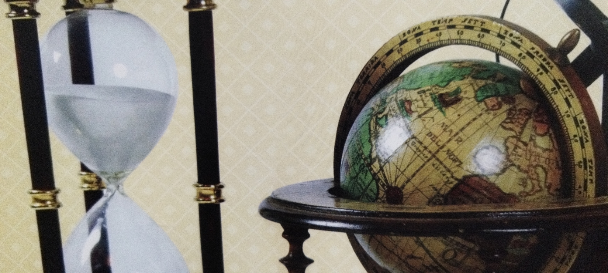 The image features a close-up, shallow-depth-of-field shot of two decorative objects against a textured, light-yellow background. On the left is a large hourglass with clear glass, filled with a shimmering, light-blue substance that occupies roughly the lower half of the bulb. The hourglass has black vertical supports with decorative gold bands. To the right, a vintage-style globe is presented. The globe is mounted on a dark wooden base with ornate legs and is enclosed by a brass meridian ring. The ring is marked with a scale, featuring text such as "TEMP SETT," "FREDDA," and numerical values. The globe itself is detailed with an old-fashioned map, showing landmasses in green and brown, and oceans with names like "MAR DEL NORT." The lighting suggests an indoor setting, possibly a study or library, with a subtle reflection visible on the globe. No people are present, and the scene appears static, focusing on the craftsmanship and aesthetic appeal of the objects. The visible text on the globe's meridian is primarily in a foreign language and relates to temperature and possibly atmospheric conditions.