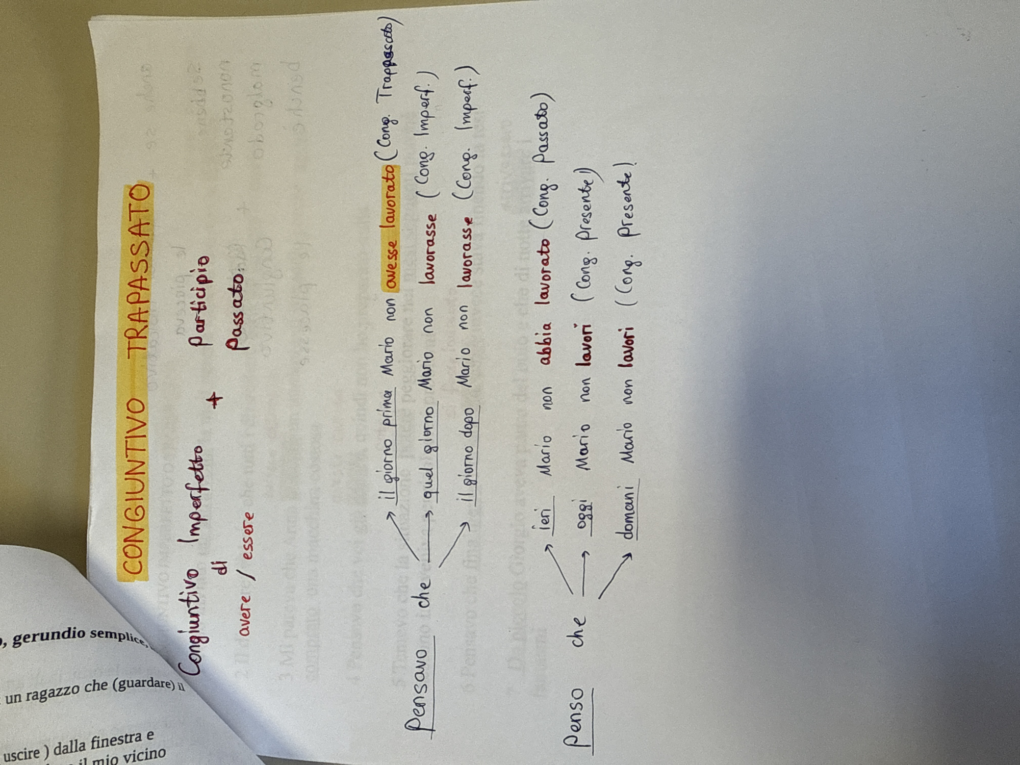 The image displays a close-up, slightly tilted view of a white sheet of paper containing handwritten notes in Italian, likely related to grammar or verb conjugation. The paper shows slight curvature on the left side, where another page of notes is partially visible. The notes are neatly written using black, red, and highlighted yellow ink.
The main subject of the notes is the "CONGIUNTIVO" (Subjunctive mood), specifically "TRAPASSATO" (Past Perfect) and "IMPERFETTO" (Imperfect). A formula "avere / essere + Participio Passato" is visible, indicating the structure for compound tenses.
Examples demonstrate the use of the subjunctive in complex sentences, starting with main clauses like "Pensavo che" (I thought that) and "Penso che" (I think that). These lead to subordinate clauses using various subjunctive tenses and temporal adverbs:
* "Pensavo che il giorno prima Mario non avesse lavorato (Cong. Trapassato)" (I thought that the day before Mario had not worked).
* "Pensavo che quel giorno Mario non lavorasse (Cong. Imperf.)" (I thought that that day Mario was not working/might not work).
* "Pensavo che il giorno dopo Mario non lavorasse (Cong. Imperf.)" (I thought that the day after Mario would not work).
* "Penso che ieri Mario non abbia lavorato (Cong. Passato)" (I think that yesterday Mario has not worked).
* "Penso che oggi Mario non lavori (Cong. Presente)" (I think that today Mario is not working/might not work).
* "Penso che domani Mario non lavori (Cong. Presente)" (I think that tomorrow Mario will not work/might not work).
The notes illustrate the sequence of tenses when using the subjunctive in Italian. The background is a plain, light-colored surface, possibly a desk or table, with minimal reflections. The overall impression is one of organized study materials.