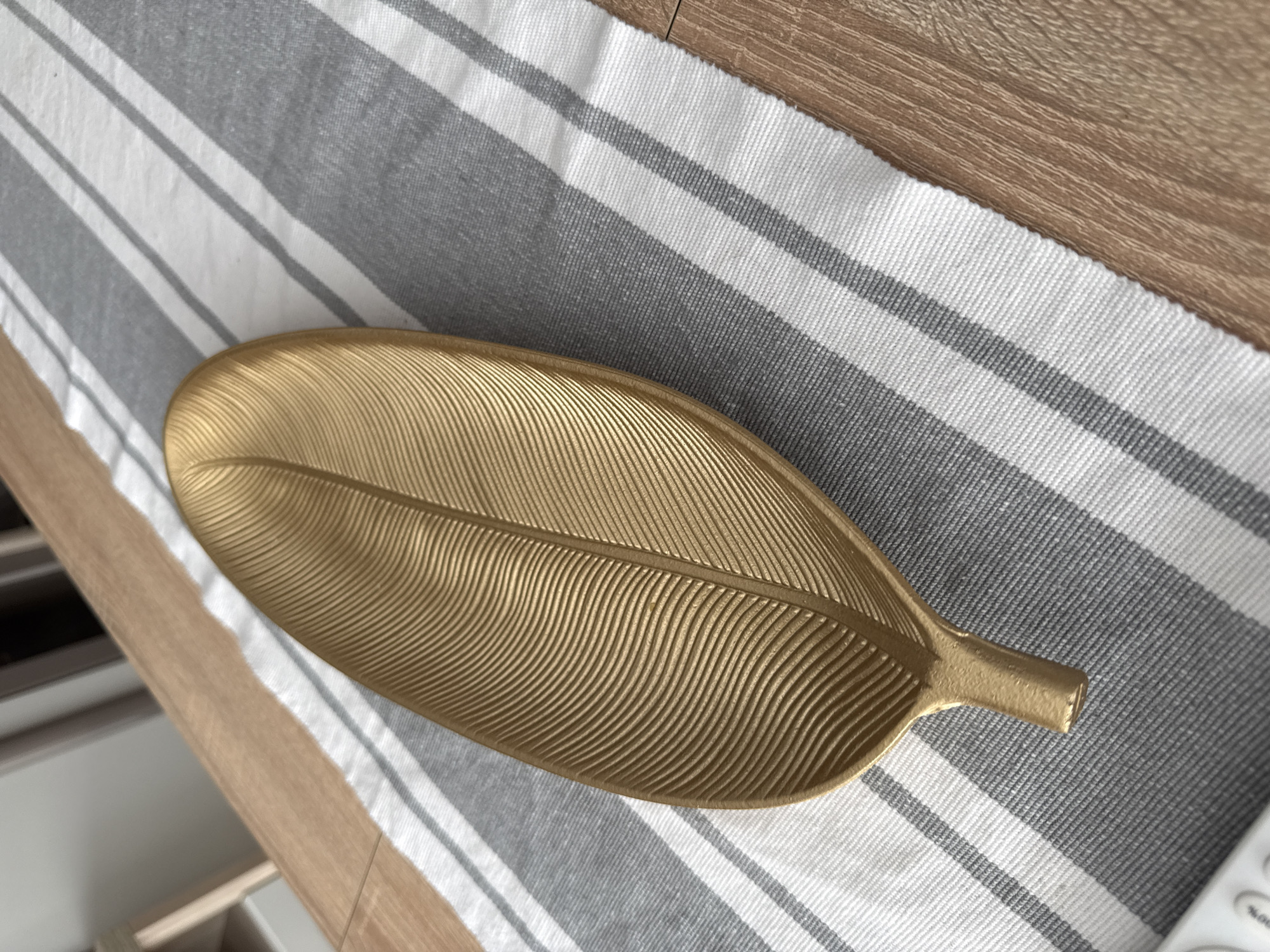 A gold, leaf-shaped decorative tray sits on a gray and white striped runner on a light wood surface. The scene appears to be indoors, likely in a residential setting. There is no indication of the location being in Lovech, Bulgaria.
