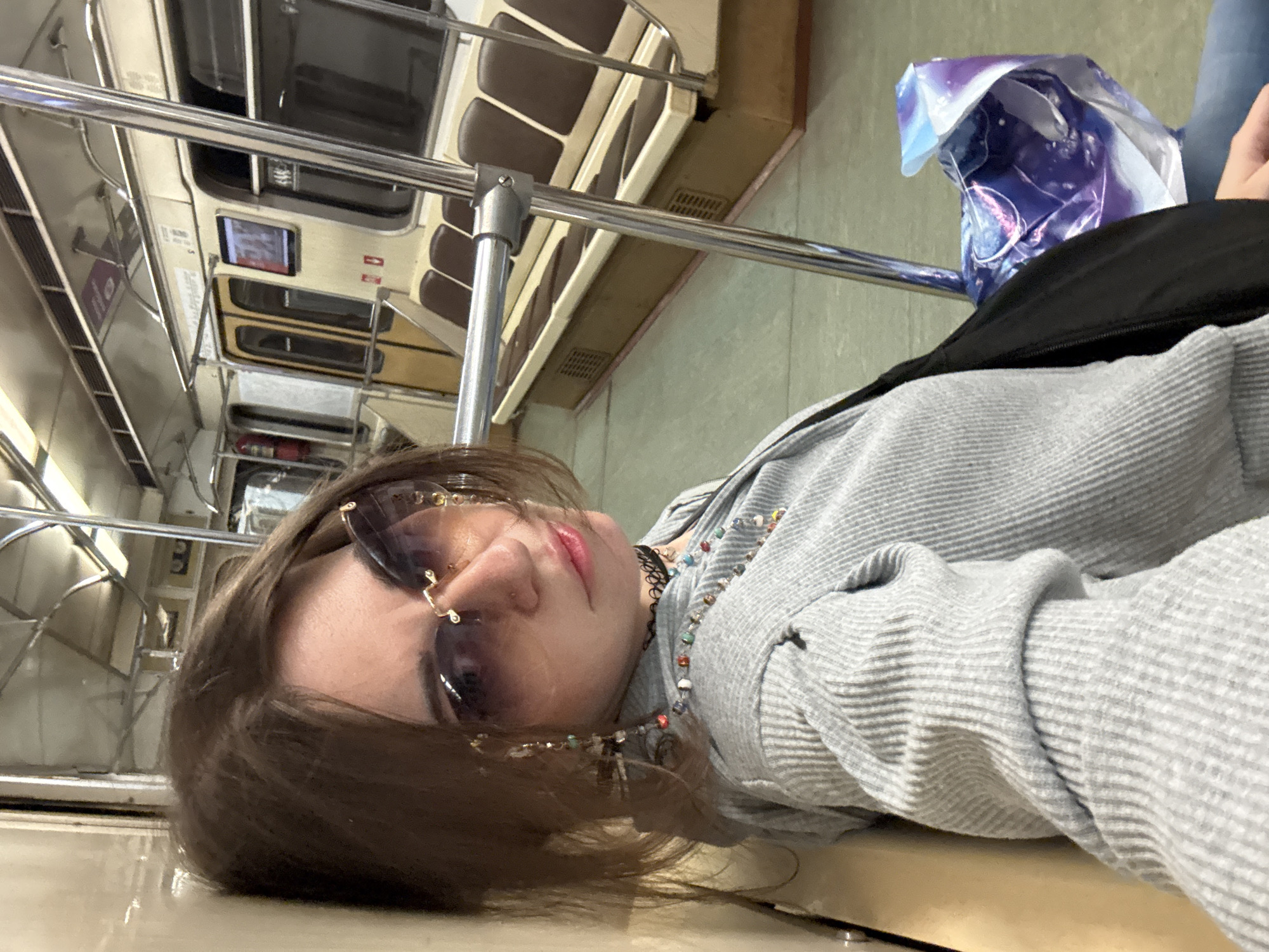 A young person is lying on a seat inside a metro car in Moscow, Russia. The metro car is an older model, with rows of brown cushioned seats. The person is wearing sunglasses and a gray striped shirt. A plastic bag is visible near the window. The image is taken from a low angle, suggesting it was taken by someone lying down.