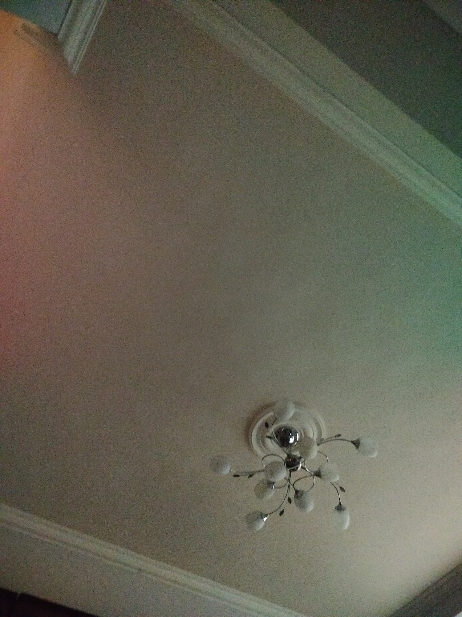 The image shows a ceiling with a light fixture in an indoor setting. The ceiling is white or a light color with molding around the edges. A chandelier-style light fixture is attached to the ceiling, featuring multiple small, round lights. The location is not discernible from the image. No people or specific actions are visible. The environment is a generic indoor space. The essential details are the ceiling, the light fixture, and the molding. There is nothing to suggest Yerevan, Armenia.