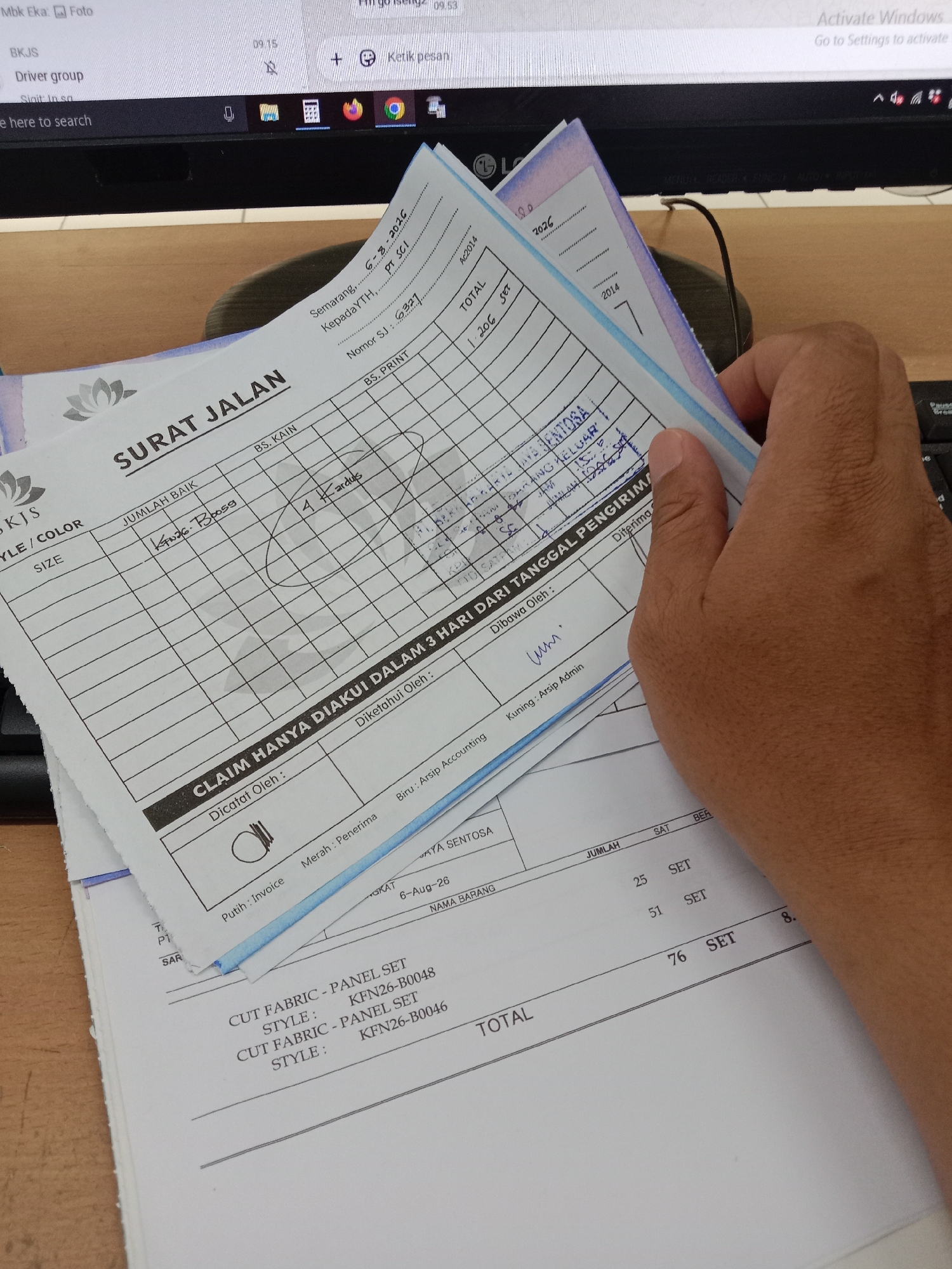 The image shows a hand holding a document titled "SURAT JALAN" (Delivery Order) which appears to be a shipping document. The document is filled with handwritten entries, including dates, numbers, and descriptions. There are several other papers beneath it. The background shows a computer monitor and a keyboard, suggesting an office or work environment. The location indicated on the document is "Semarang, 6-3-2016", suggesting the document was processed in Semarang, Indonesia on March 6, 2016. The items listed on the document are "CUT FABRIC - PANEL SET" with style numbers like "KFN26-B0048" and "KFN26-B0046". The context implies a logistics or inventory management scenario.