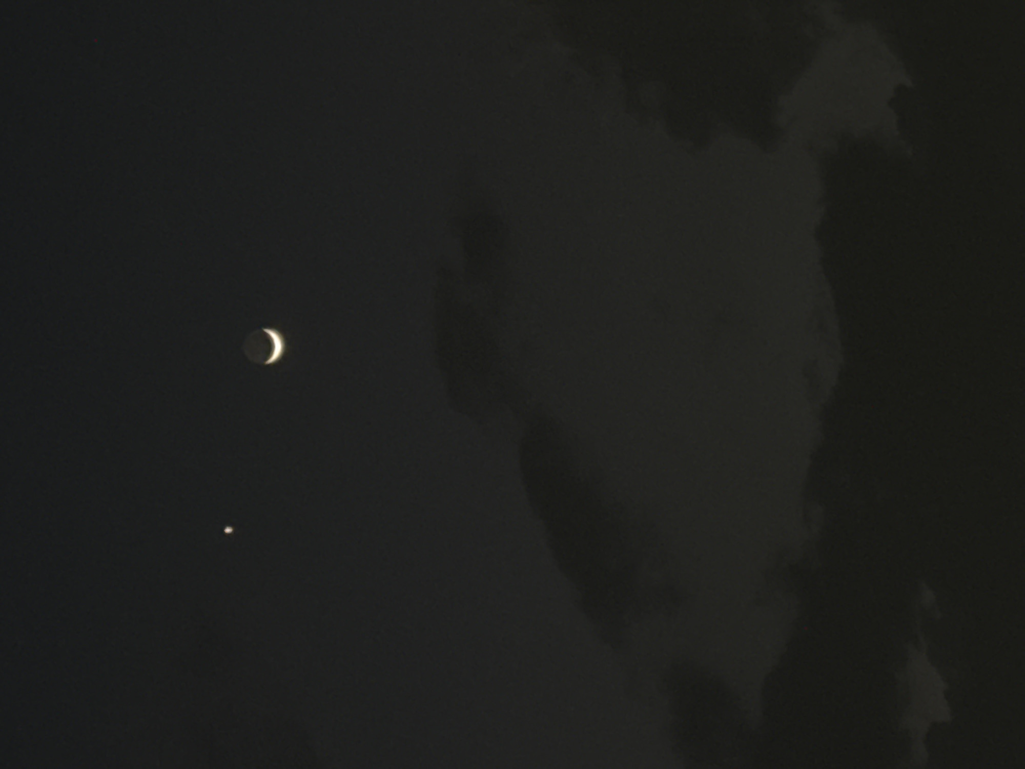 A dark nighttime scene with a crescent moon and a bright object, likely a planet or star, visible in the upper left quadrant. To the right are dark, indistinct cloud formations. No people or any identifiable objects or location in San Bernardino Tlaxcalancingo, Mexico are visible.