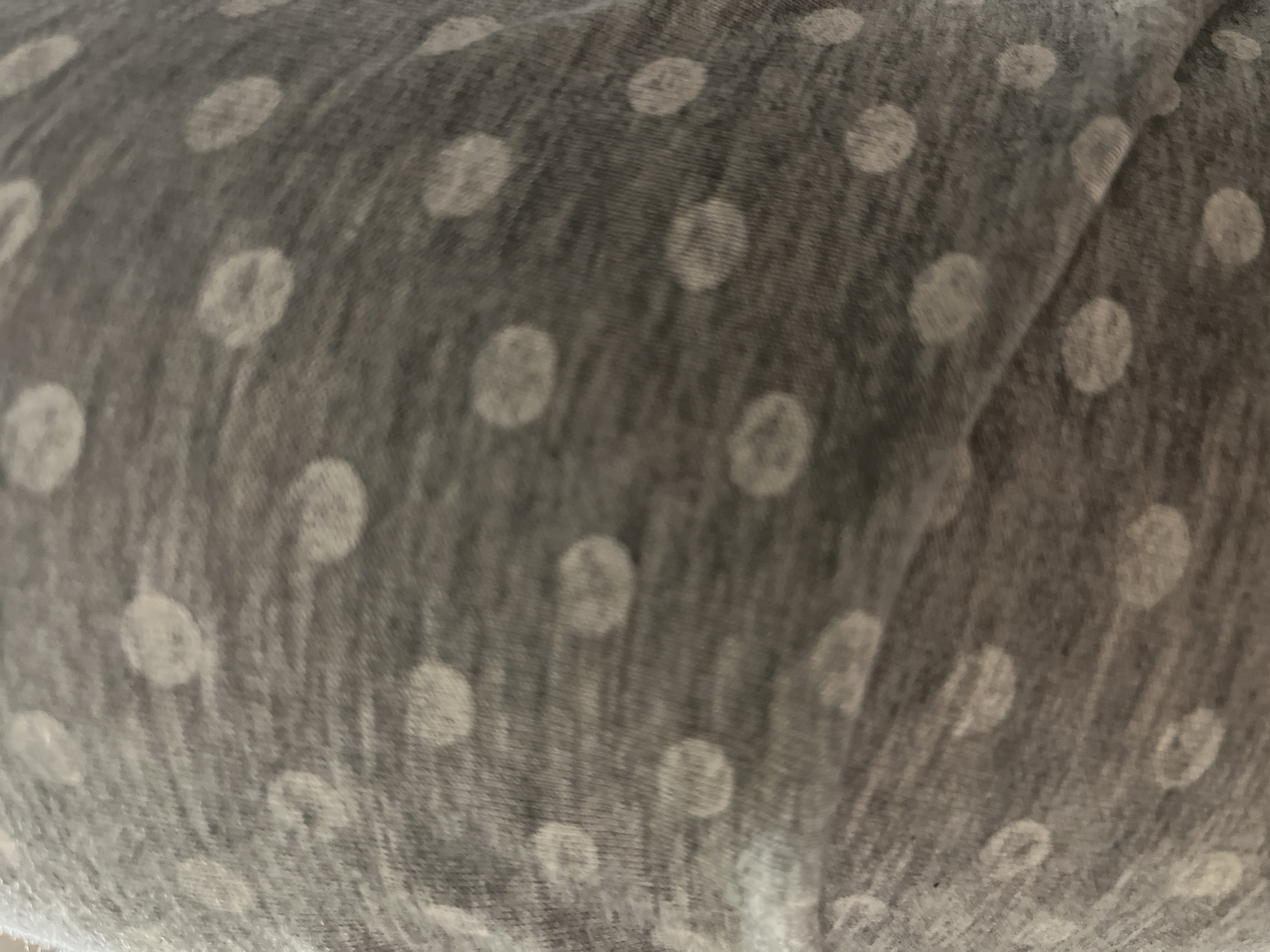 The image shows a close-up of a gray fabric with white polka dots. The fabric appears slightly wrinkled or creased. The polka dots are evenly distributed across the surface.