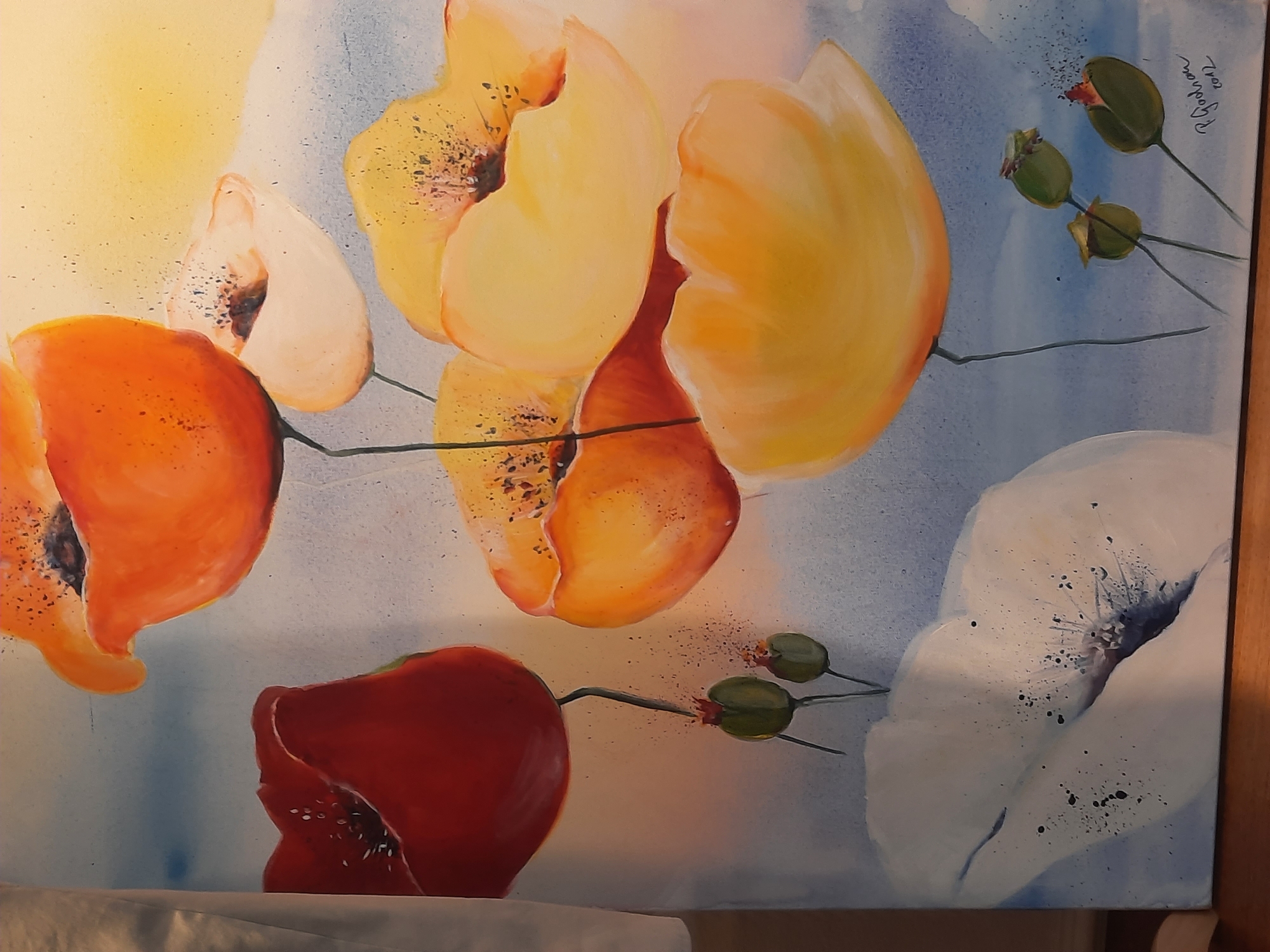 This is a photograph of a watercolor painting featuring a cluster of poppies in various shades of red, orange, yellow, and white, set against a soft blue and yellow background. Several poppy buds are also depicted. The painting is signed "P. Gudrun 2012" in the lower right corner. The location of this painting within Rosenheim, Germany is not discernible from the image. The photograph itself appears to be taken indoors, with some soft lighting and a hint of fabric to the left.