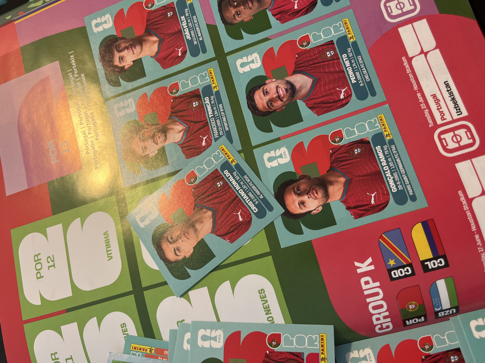 The image shows a collection of Panini football stickers and a promotional sheet, presumably for a FIFA tournament. The stickers feature Portuguese national team players including Cristiano Ronaldo, João Félix, Pedro Neto, Francisco Trincão, and Gonçalo Ramos. The promotional sheet displays the Portuguese flag, along with flags of Uzbekistan, Colombia, and Democratic Republic of the Congo, categorized under "Group K". A text segment indicates match dates and location: "Tuesday, 23 June - Houston Stadium" and "Wednesday, 17 June - Houston Stadium", Portugal vs. Uzbekistan. The text on the promotional sheet also includes "POR 12" and "VITINHA". There is no evidence to suggest that the location is in San Bernardino Tlaxcalancingo, Mexico.