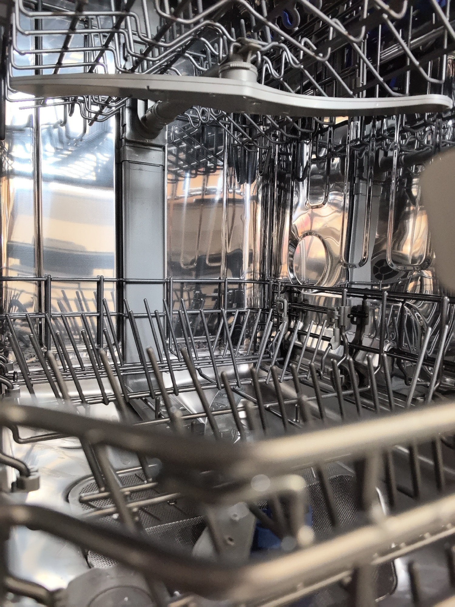 The image shows the interior of a dishwasher. It's a close-up shot focusing on the racks and spray arm. The interior walls of the dishwasher are shiny and reflective. The racks are made of metal and have rows of tines for holding dishes. A spray arm is visible at the top of the frame. The location in the city of Фролы, Russia is extraneous information as it cannot be determined from the image itself.