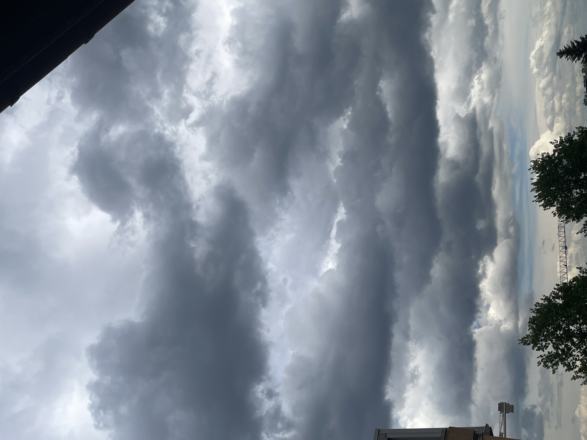 The image shows a sky filled with dark, ominous clouds, suggesting an approaching storm or recent rainfall. There are trees and buildings at the bottom of the frame.