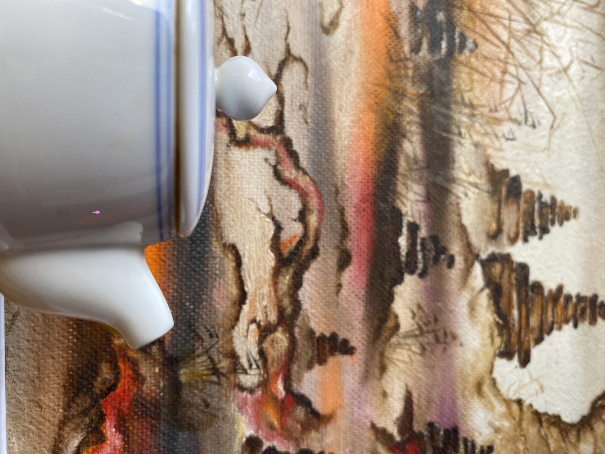A close-up image shows a white ceramic object with blue stripes on the left side of the frame. The ceramic object also has a small, rounded handle. The background is a textured surface with a painting or print featuring a variety of colors, including browns, oranges, reds, and grays. The painting depicts abstract shapes resembling branches, trees, or geological formations. The exact location in the city of Chaikovsky, Russia, is not evident from the image. There are no discernible people or actions captured in this image.