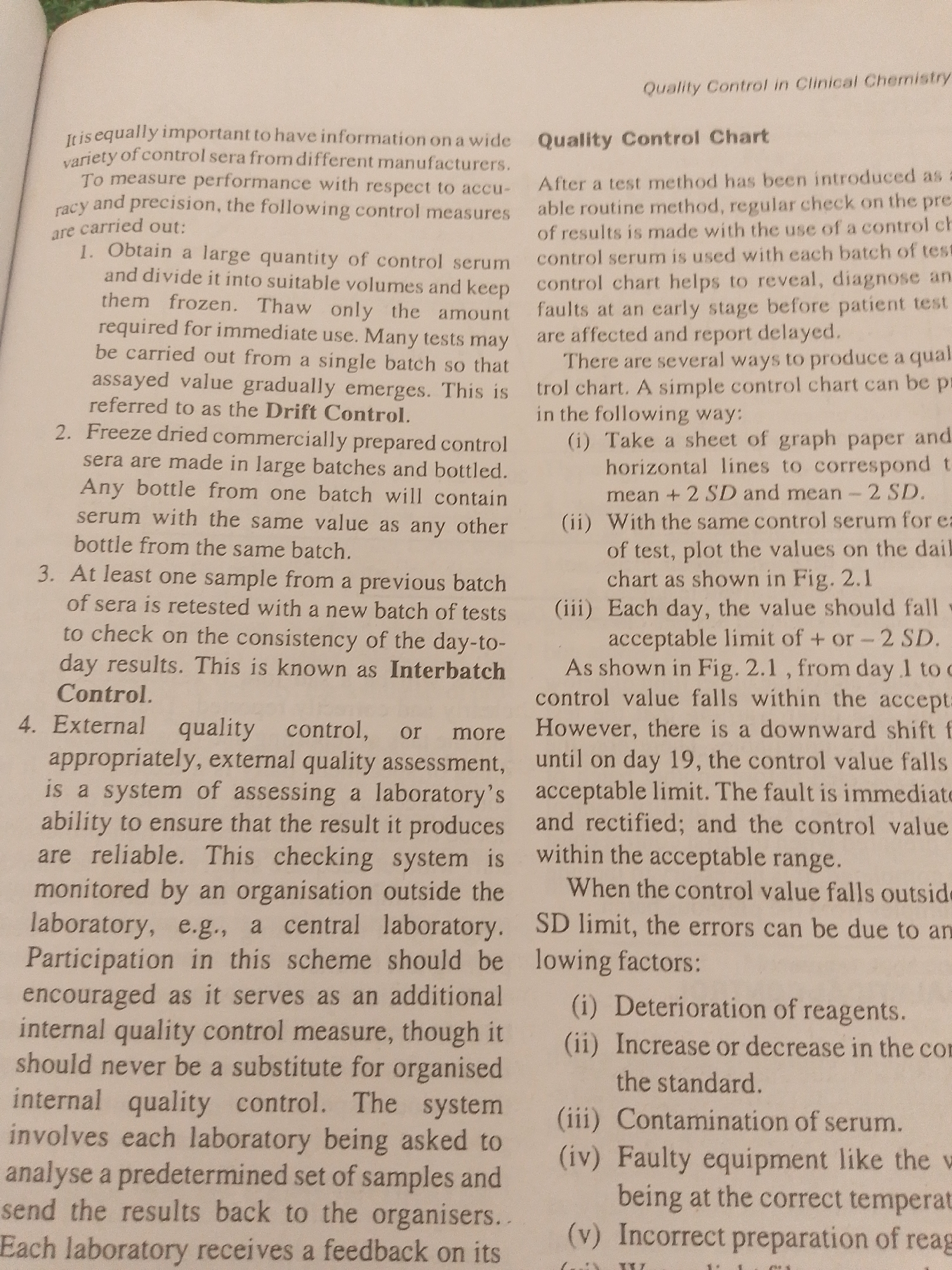 This media file is a photograph of an open textbook page, viewed from a slightly oblique angle. The page is filled with text, primarily in English, discussing quality control in clinical chemistry. The text is organized into titled sections and numbered lists, indicating a practical or educational context.
The main subjects are the printed words themselves, arranged in paragraphs and bullet points. There are no people or objects other than the book and the surrounding environment, which is out of focus. The setting appears to be an indoor location, likely a library or study area, given the nature of the content.
The activity taking place is implied to be reading or studying. The page itself is the sole focus, and no actions are directly depicted.
Notable details include the title "Quality Control in Clinical Chemistry" at the top right and "Quality Control Chart" as a prominent heading. Several numbered points outline methods and concepts related to quality control, such as "Drift Control," "Interbatch Control," and steps for creating a control chart, including plotting values on a graph paper with "mean + 2 SD" and "mean - 2 SD" lines. The text also lists potential reasons for control values falling outside acceptable limits, such as "Deterioration of reagents" and "Contamination of serum." The lighting appears to be artificial, casting a slight shadow on the right side of the page. There are no overt emotional cues as it is an inanimate object. The location context of Jalingo, Nigeria, is not discernible from the image itself, as there are no visual cues related to that specific place.