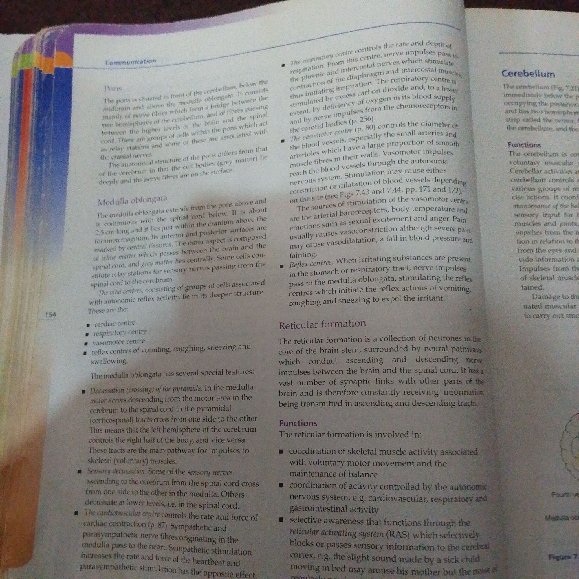 The image displays an open textbook with text related to the human brain and nervous system. The book is open to a page discussing the pons, medulla oblongata, cerebellum, and reticular formation. Several headings and bullet points are visible, detailing the functions and anatomical features of these brain regions.
The text on the left page describes the pons as being situated in front of the cerebellum and above the medulla oblongata, consisting of nerve fibers that form a bridge between the two hemispheres of the cerebellum and the spinal cord. It also mentions the medulla oblongata extending from the pons above and the spinal cord below, and its role in vital centers and reflex activities.
The right page focuses on the cerebellum, describing its location and function in controlling voluntary muscular and cerebellar activities. It also details the functions of the reticular formation, including coordination of skeletal muscle activity, maintenance of balance, and selective awareness of sensory information. A diagram of the cerebellum is partially visible at the bottom right, labeled as "Figure 7.21".
The overall scene is of an academic setting, likely a library or study area, with the textbook laid open for reading or reference. The lighting suggests an indoor environment, possibly during daylight hours, though no specific time of day or weather conditions are evident. The context of Jalingo, Nigeria, is provided, but there are no visual cues within the image to confirm this specific location. The focus is purely on the educational content presented in the textbook.