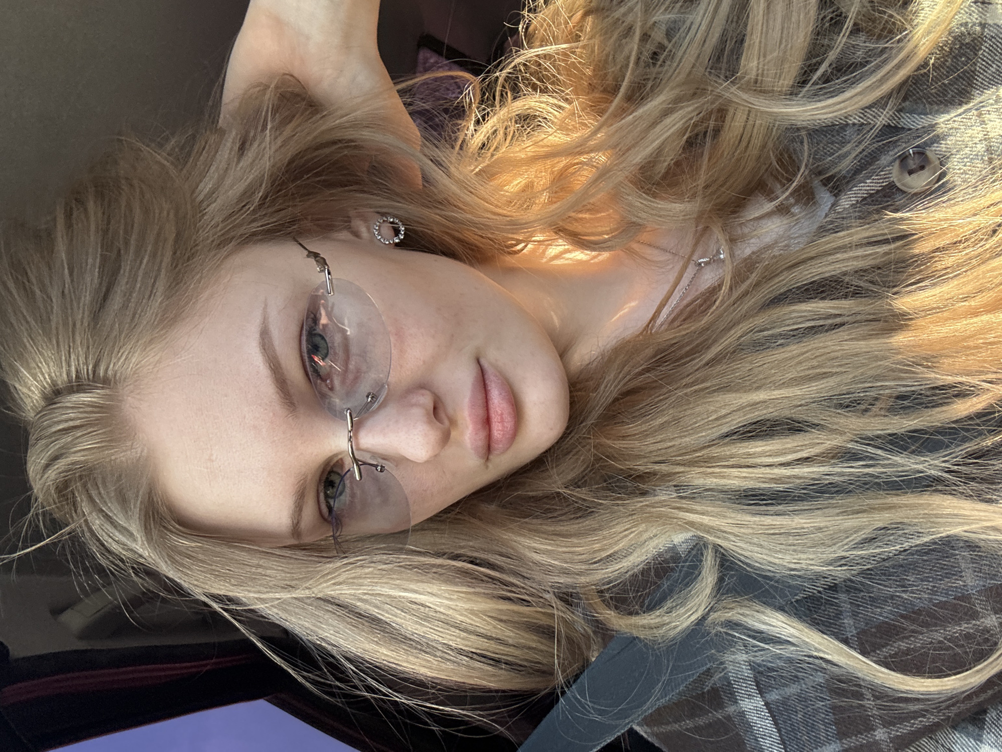 A young woman with blonde hair is pictured in a close-up selfie, likely taken inside a car. She is wearing rimless glasses and a plaid shirt. The location is potentially Perm, Russia, but this information is not directly discernible from the image itself and would require additional context or metadata to confirm.