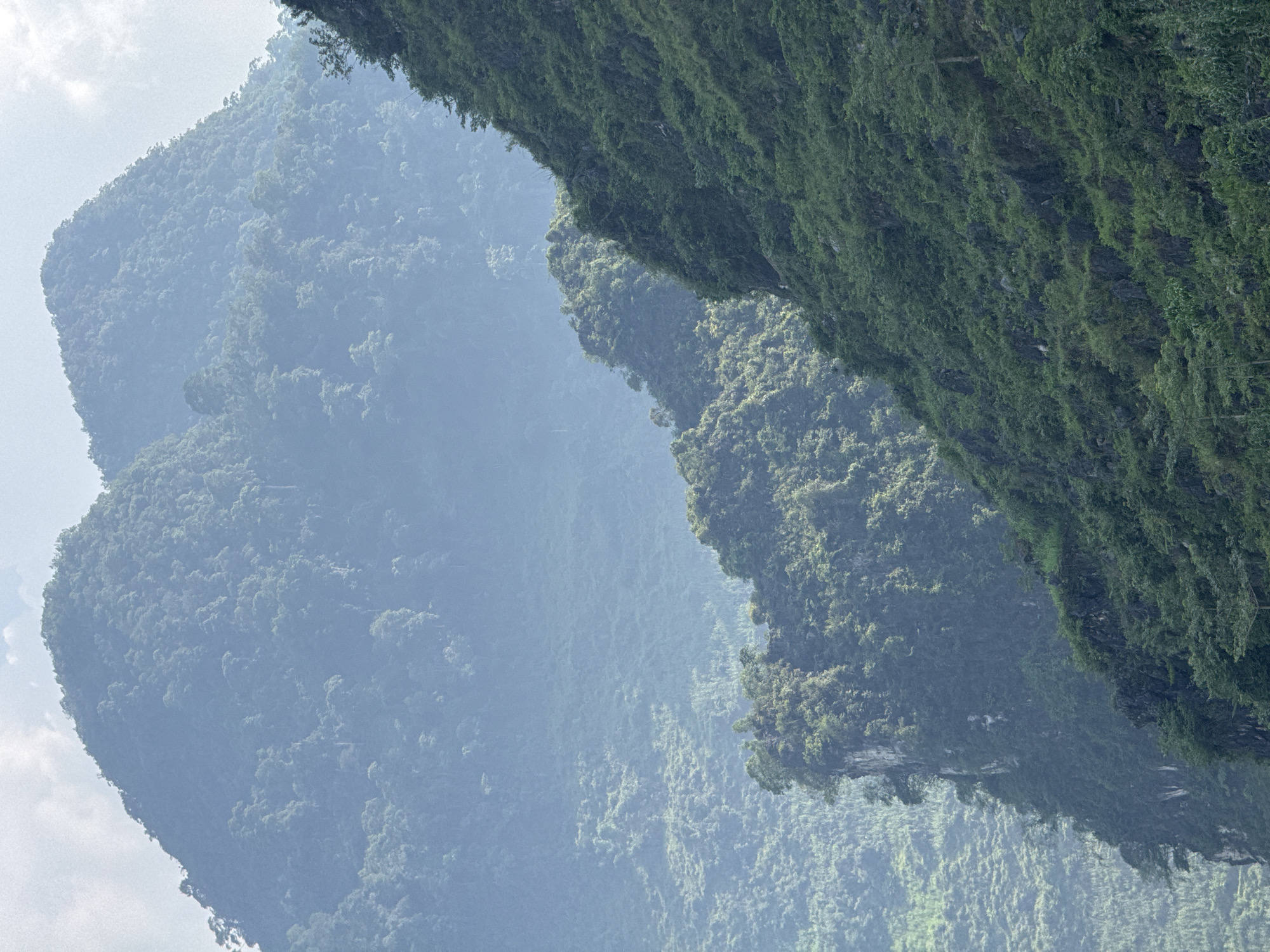 The image shows a mountainous landscape in Đường Thượng Commune, Vietnam. Lush, green vegetation covers the steep mountain slopes. The peaks are shrouded in mist, creating a hazy, layered effect. The sky is overcast. No people or animals are visible.