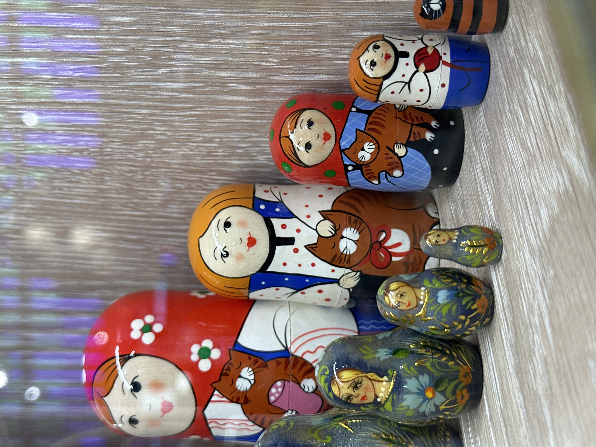 The image shows a collection of Russian nesting dolls (Matryoshka dolls) of various sizes arranged on a wooden surface. The dolls are painted with traditional designs of women and cats. The location in Khimki, Russia is not directly discernible from the visual information in the image.
