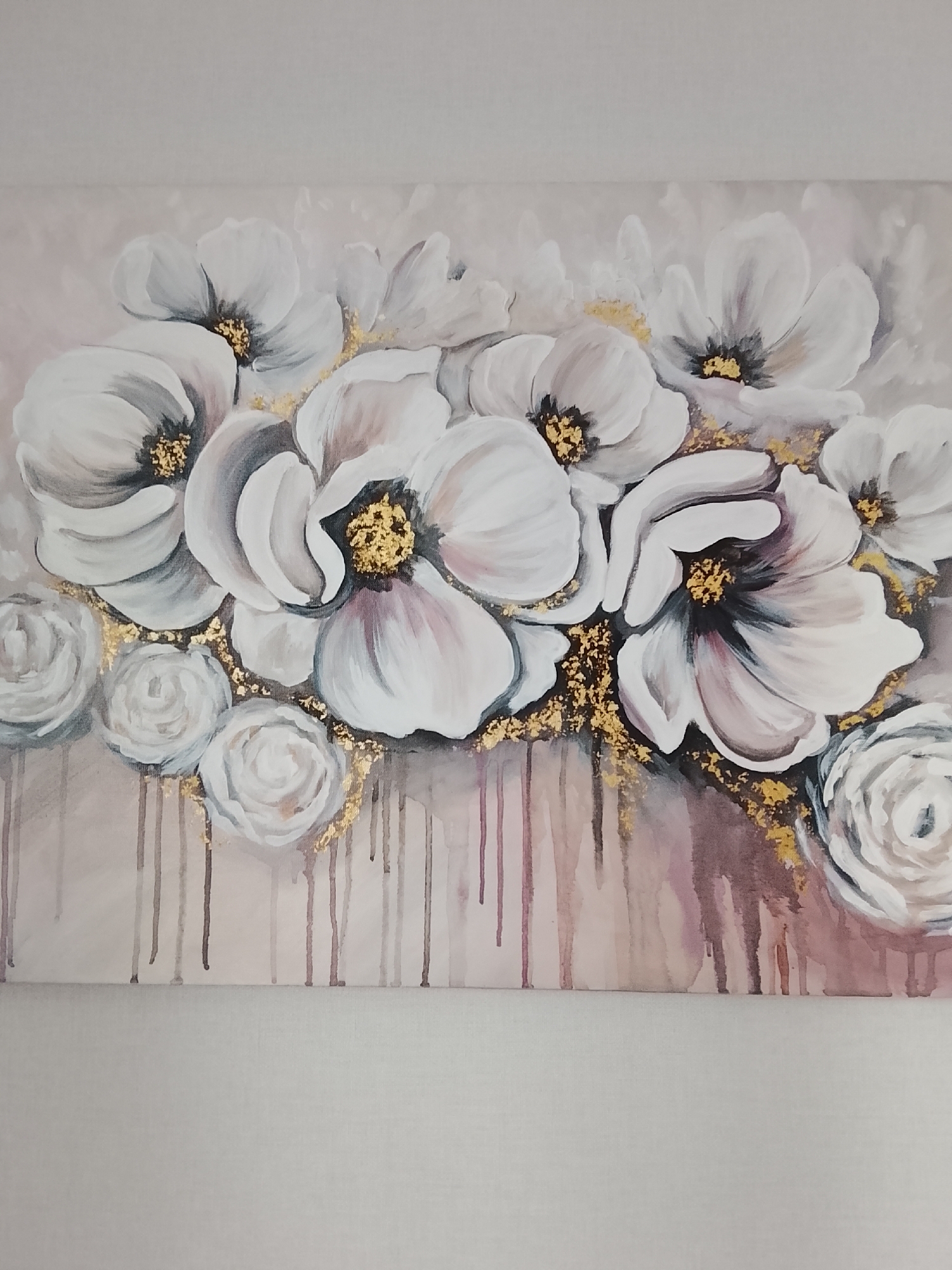 A painting on canvas features a bouquet of white flowers with gold accents against a light pink background. The flowers, primarily large, open blooms with darker centers, are clustered towards the top of the canvas. Smaller, rose-like buds are visible at the bottom left and right. Dripping paint in shades of pink and brown creates a vertical, watercolor-like effect at the bottom of the bouquet. The painting is displayed on a plain, light-colored wall, suggesting it is likely an indoor scene. There is no information available about its location in the city of Miniino, Russia.