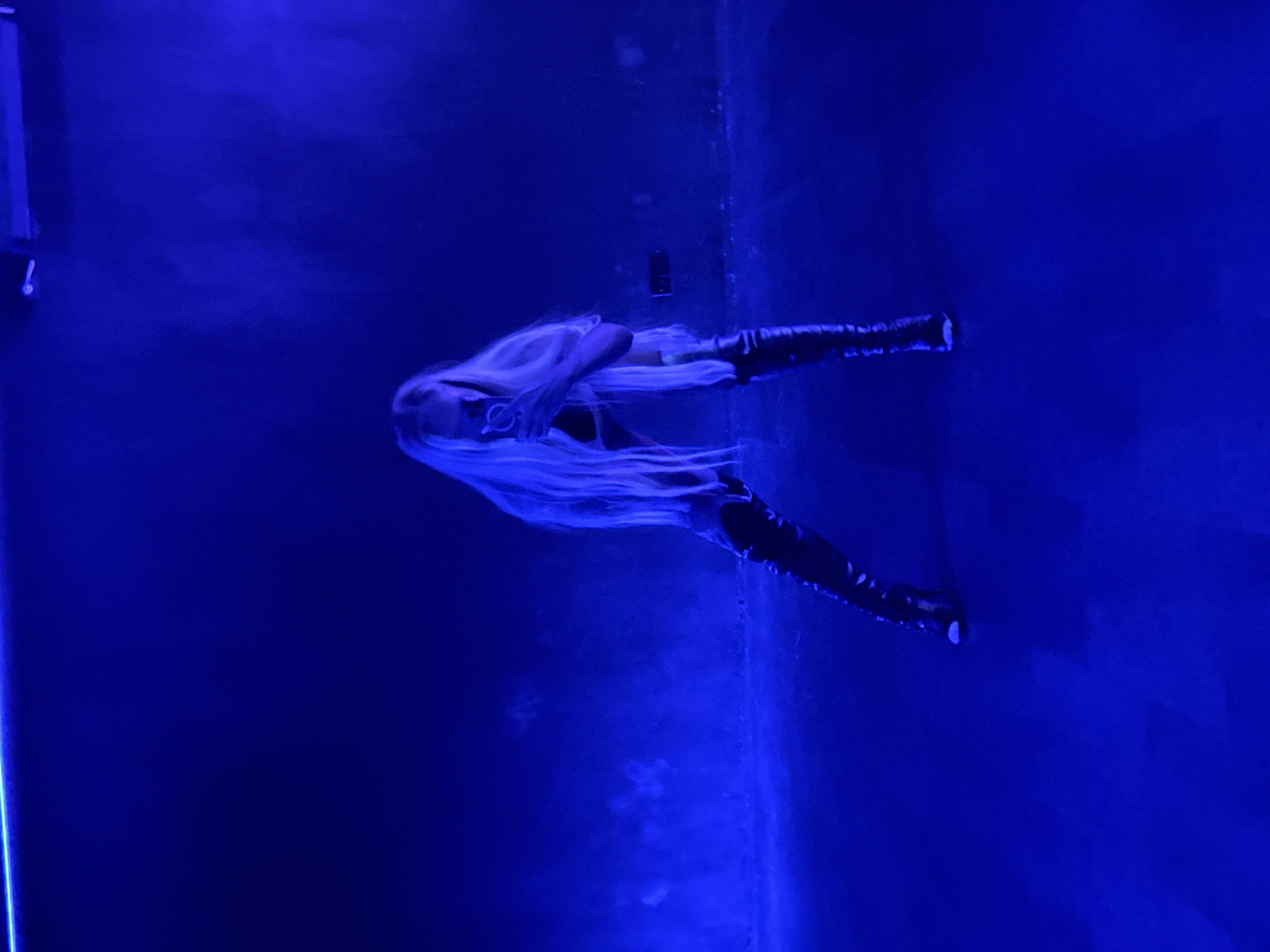 A woman with long, blond hair, wearing black boots, is positioned in a room with blue lighting. A phone is attached to the wall. The location is not specified, and the North Kuta, Indonesia, location claim is not corroborated in the image.