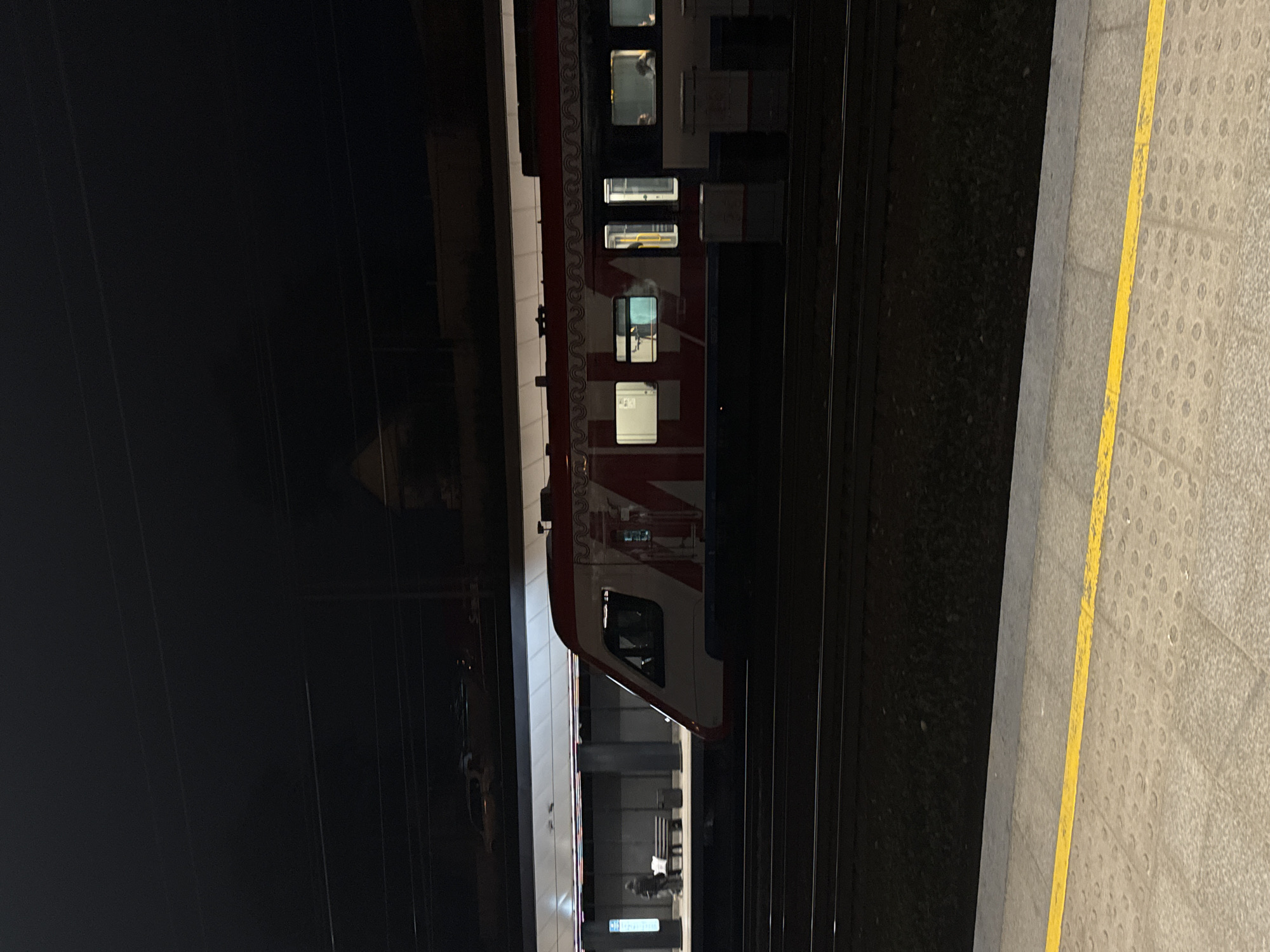 A train sits at a station platform. The train is white and red and has windows along the side. The platform is gray and has a yellow line. The environment is dark. The location is Moscow, Russia.