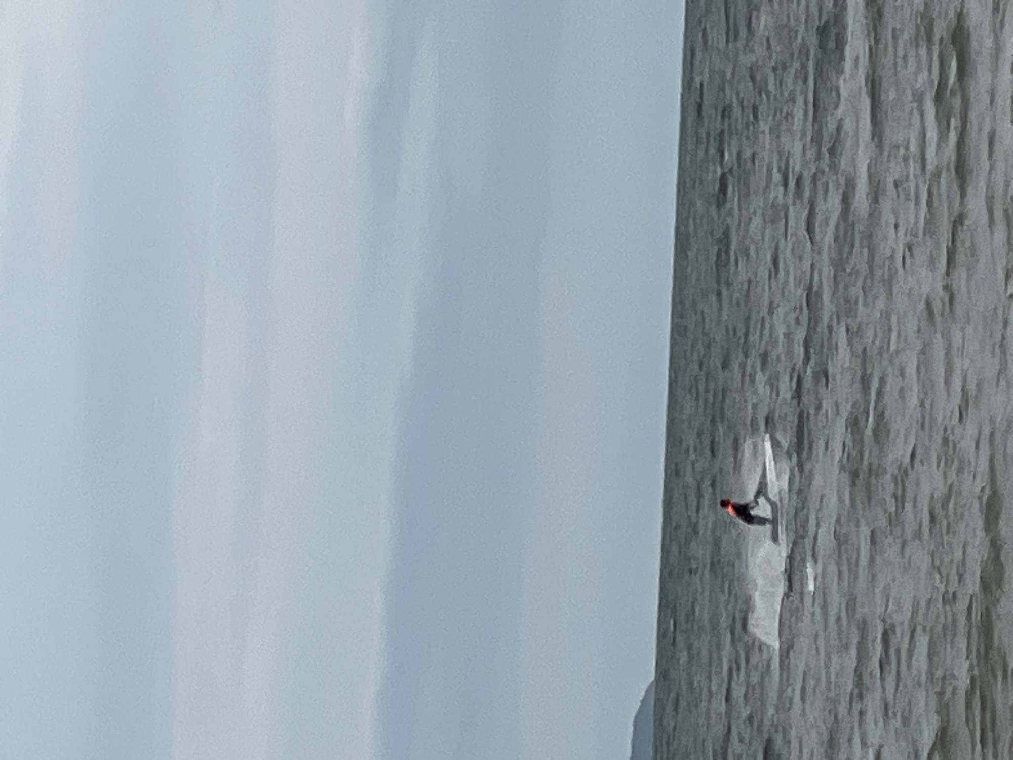 A person on a jet ski is riding on a dark, choppy body of water. The person is wearing a bright orange vest. The sky is overcast and a faint line of land is visible on the horizon to the left. The image does not contain any recognizable landmarks or features that would indicate it is located in Pattaya City, Thailand.