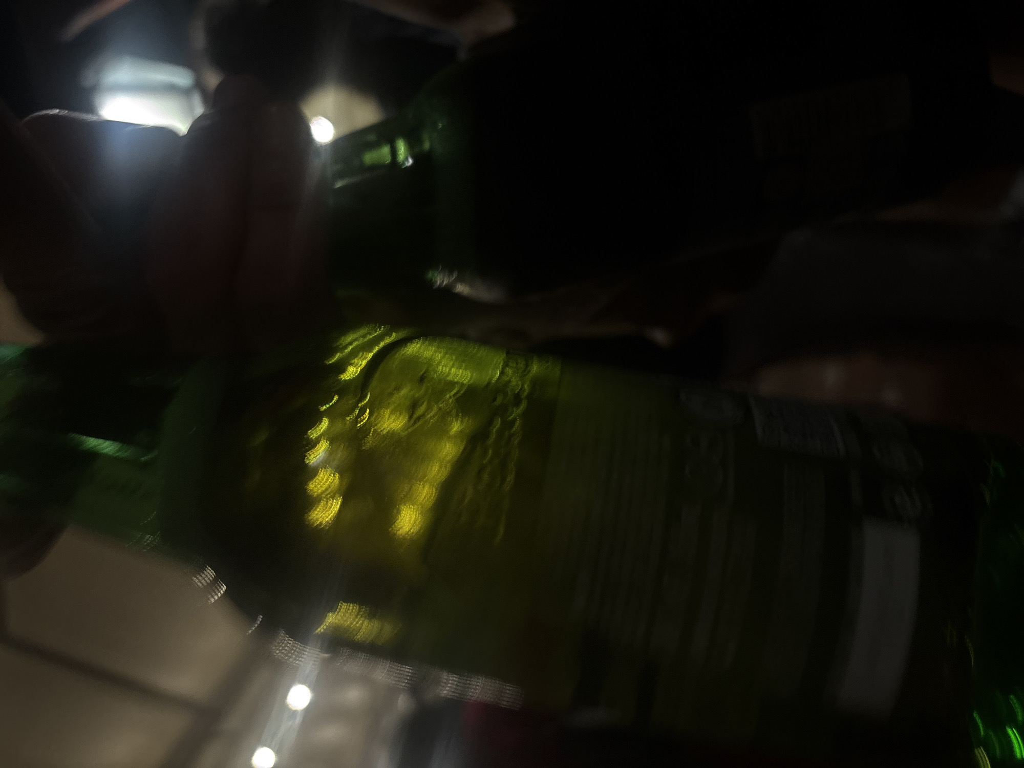 The image shows two green beer bottles, one in the foreground and one in the background. A hand is holding the foreground bottle. The photo appears to be taken indoors, with lights visible in the background. Location details related to Mexico City, Mexico, are not discernible from the image.