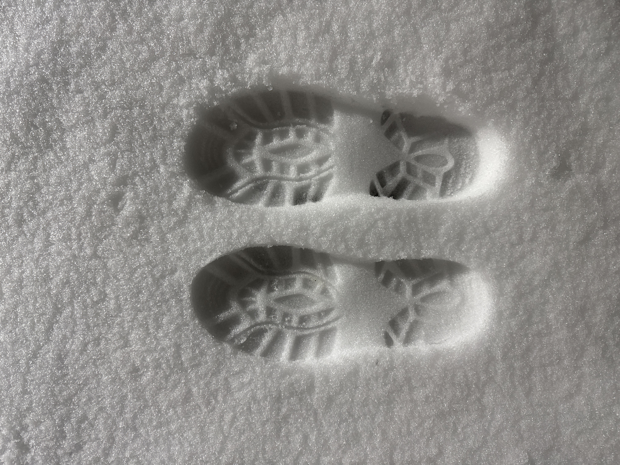 The image shows two clear footprints in fresh, undisturbed snow. The location is not discernible from the image and cannot be determined to be in Вассята, Russia. The footprints are from a shoe or boot with a distinct tread pattern, including a circular design on the heel. The snow appears powdery and the footprints are well-defined, suggesting recent activity. No people or other objects are visible beyond the snow and footprints.