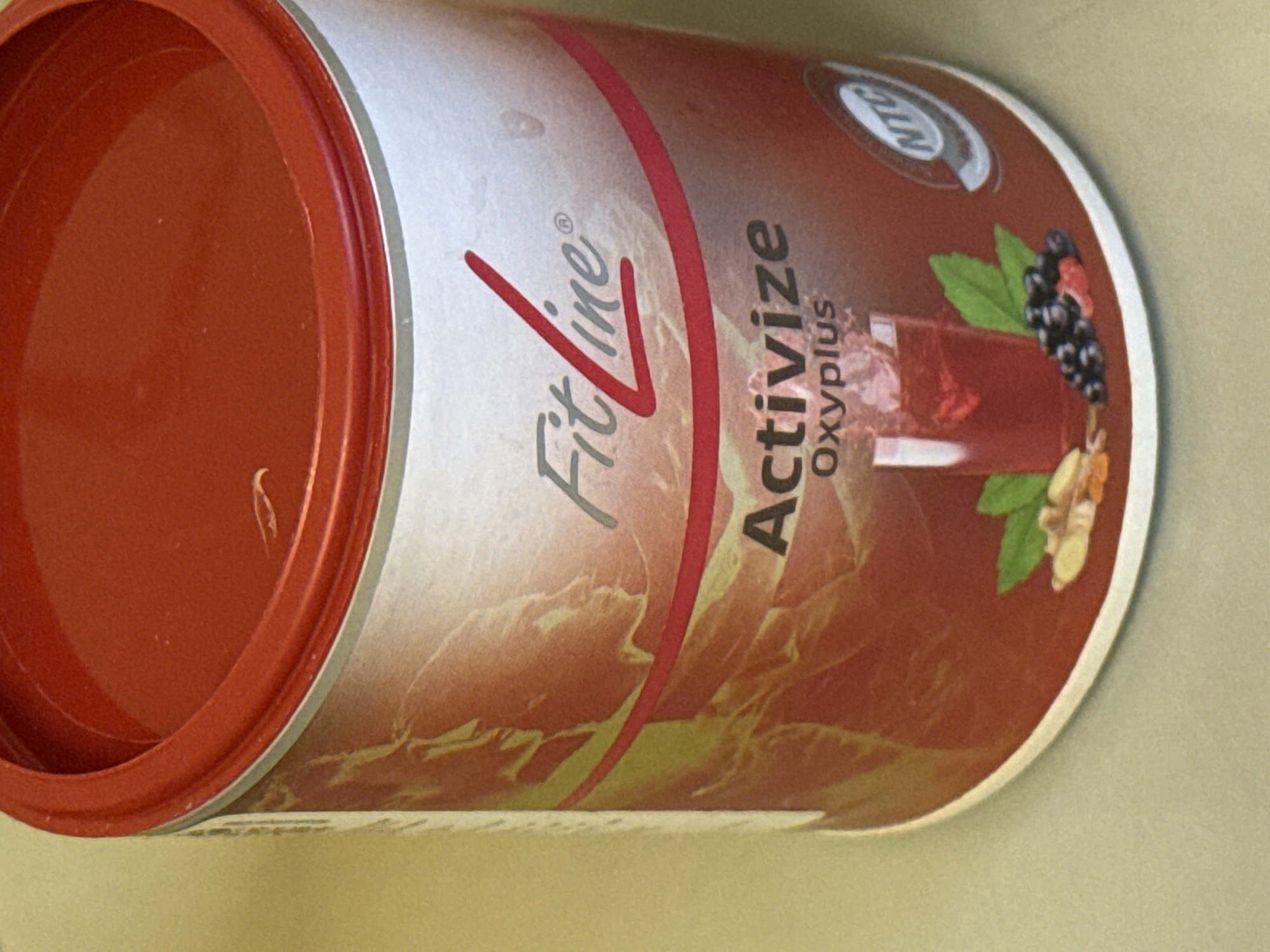 The image shows a canister of FitLine Activize Oxyplus dietary supplement. The canister is predominantly silver and red in color, with an illustration of berries and a glass of liquid. The canister is positioned on a light-colored surface. The specific location in Novo-Nikol'skoe, Russia is not identifiable from this image.