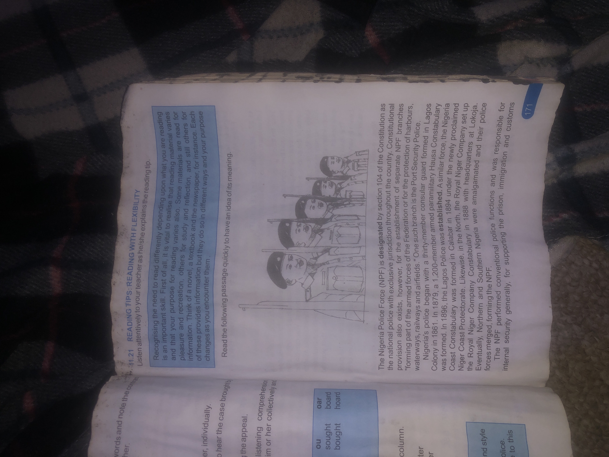 The image shows an open book with text and an illustration. The text is in English and appears to be from an educational book. The title of the section is "READING TIPS: READING WITH FLEXIBILITY." There is an illustration of five uniformed men with rifles. The text discusses the history of the Nigeria Police Force (NPF). There is no indication of the city of Jalingo, Nigeria, or any specific location within it. The scene is entirely within the context of a book, not a real-world environment.
