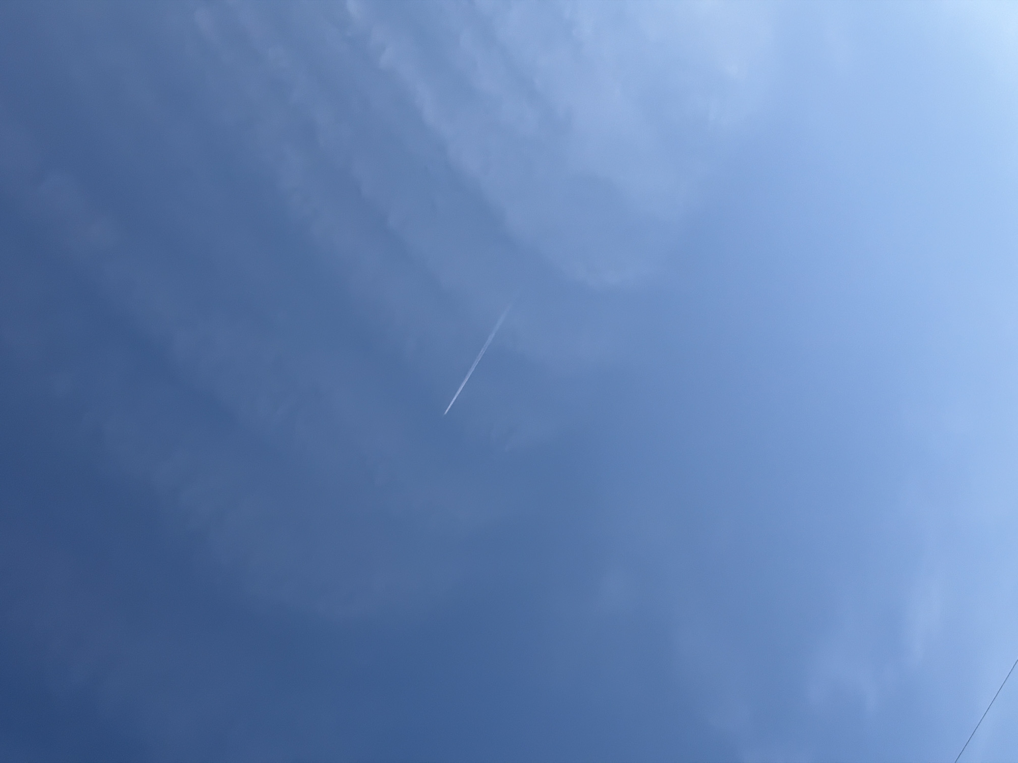 The image shows a blue sky with wispy clouds. A contrail is visible, likely from an airplane. The location is not identifiable as Chaikovsky, Russia, based on the image alone. No people or objects other than the sky, clouds, and contrail are present. There are no visible actions or interactions occurring.