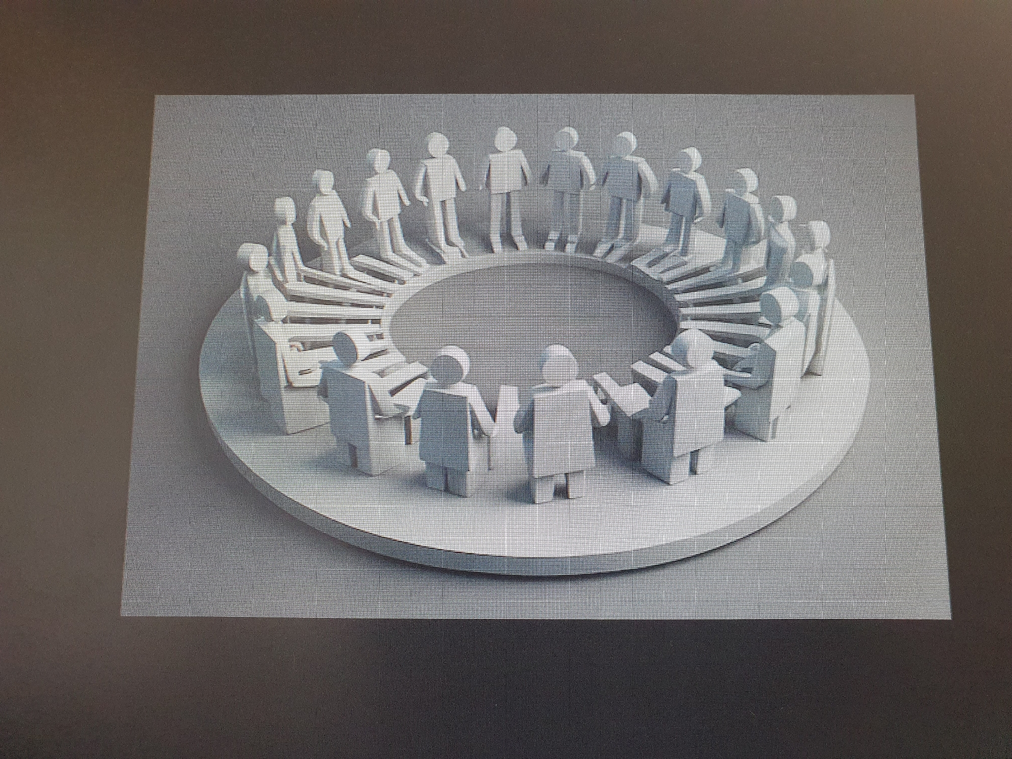 The image shows a circular arrangement of white, stylized human figures. The figures appear to be standing on a tiered, circular platform, with some figures on a lower level and others on a higher level, forming concentric rings. The figures are abstract, with simple, block-like forms representing heads, torsos, and limbs. Some figures are facing inwards, towards the center of the circle, while others are facing outwards. The overall impression is one of a gathering or a meeting. The image is a photograph of a screen, with the textured surface of the screen visible. There is no information in the image to indicate a location in Tashkent, Uzbekistan.