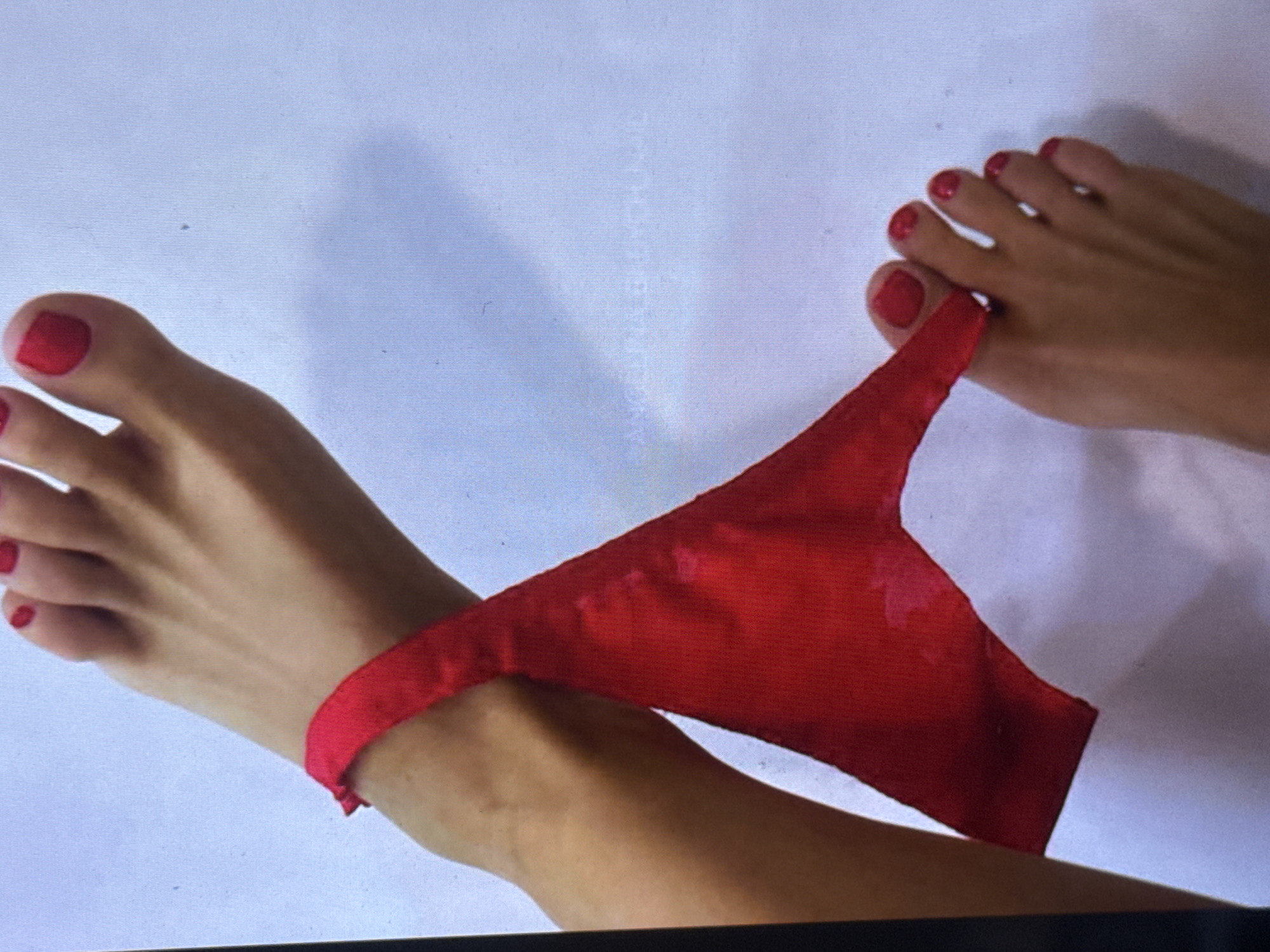 Two bare feet with red nail polish are visible against a white background. A red thong is draped around one ankle and over the toes of the other foot. The image does not provide information about the location in Kuta Selatan, Indonesia.