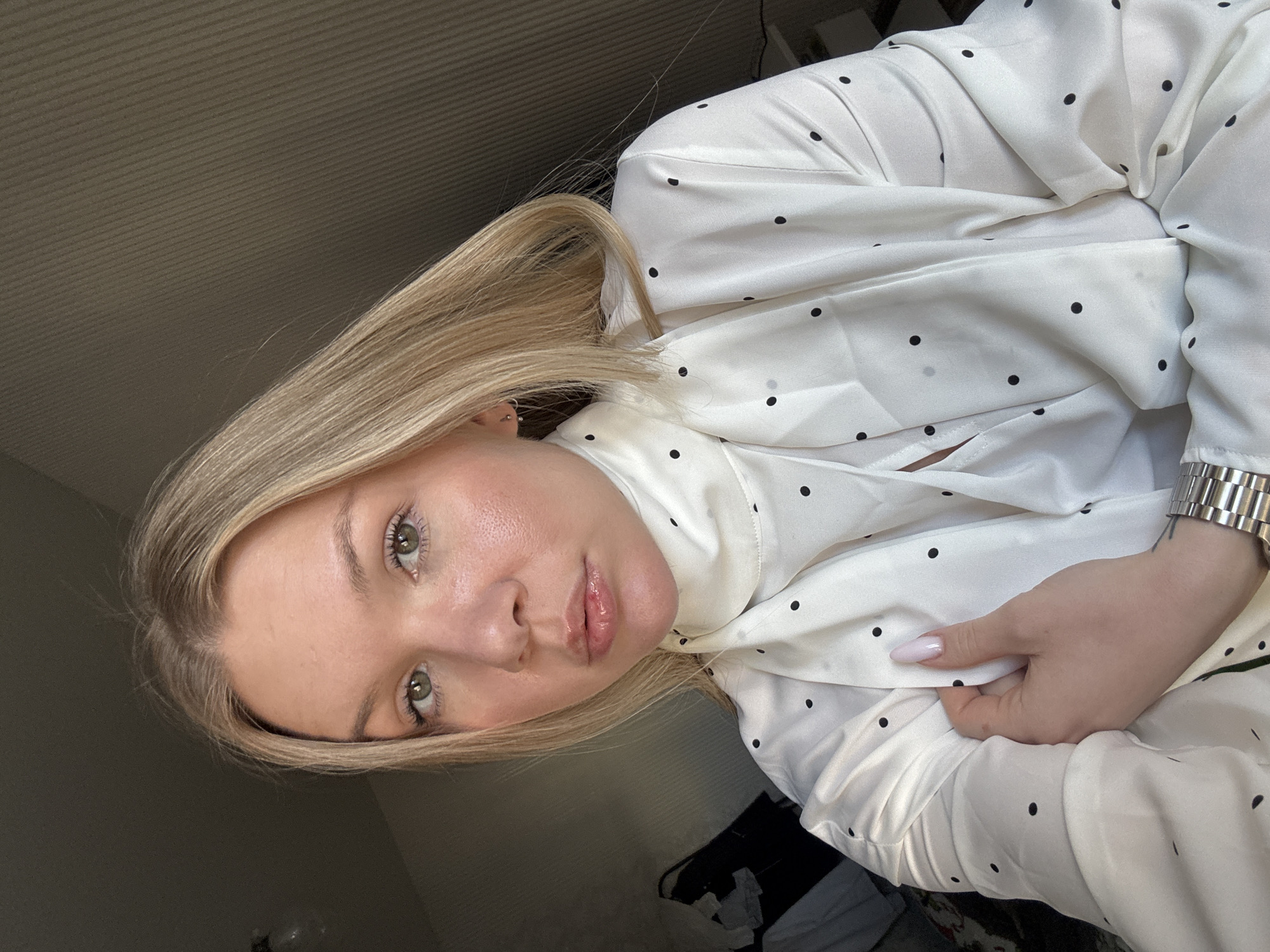 A blonde woman with fair skin is shown in a selfie-style portrait. She has green eyes and full lips. She is wearing a white blouse with black polka dots. The image is taken indoors. There is no evidence to confirm the location is Perm, Russia.