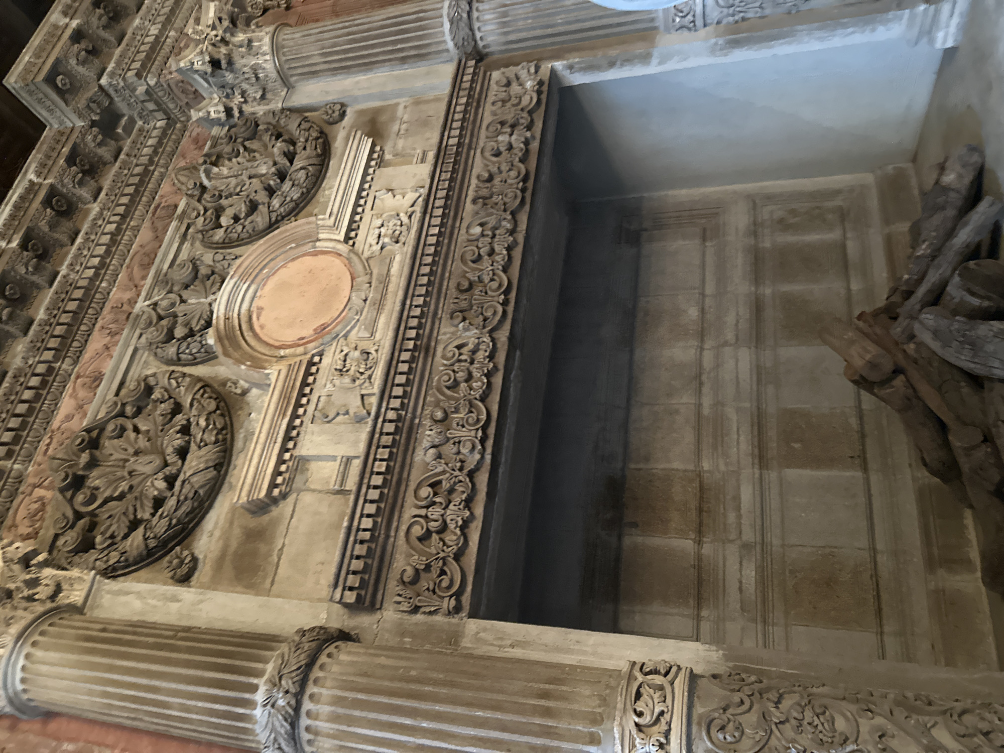 The image shows a detailed view of ornate architectural elements, likely part of a building's facade or interior in Tlalnepantla, Mexico. The architecture features carved stone, decorative columns, and intricate moldings. The right side shows a recessed area with stone walls and what appears to be wooden planks or beams piled within the space. There are no people visible.