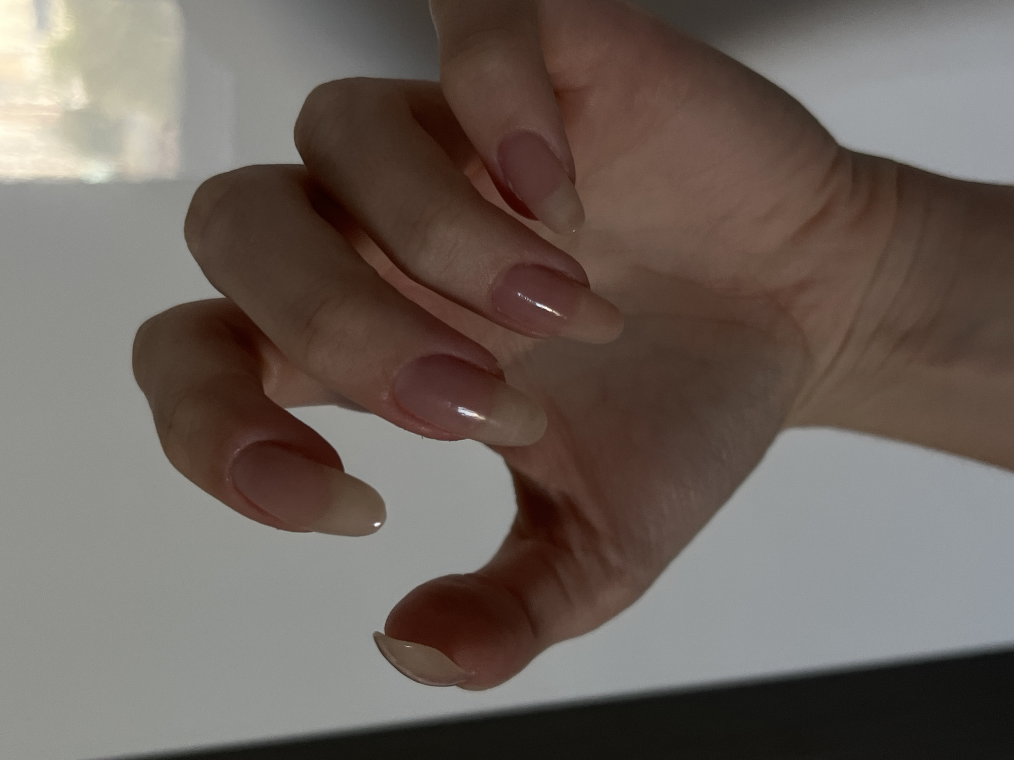 The image shows a close-up of a person's hand with manicured nails. The nails are oval-shaped and appear to have a light pink or nude polish. The hand is positioned in a relaxed, slightly curled pose against a plain, light-colored background. The lighting is soft, creating subtle shadows that highlight the contours of the hand and nails. There is no indication of the location in Chelyabinsk, Russia, or any other environmental details.