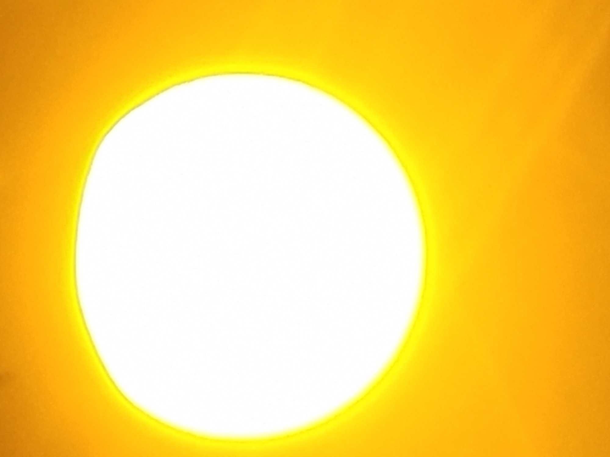 The image shows a bright, white, irregularly shaped circle surrounded by a yellow background. The circle has a glowing, yellowish halo around its perimeter. The image appears to be overexposed, with the yellow background also appearing quite bright.