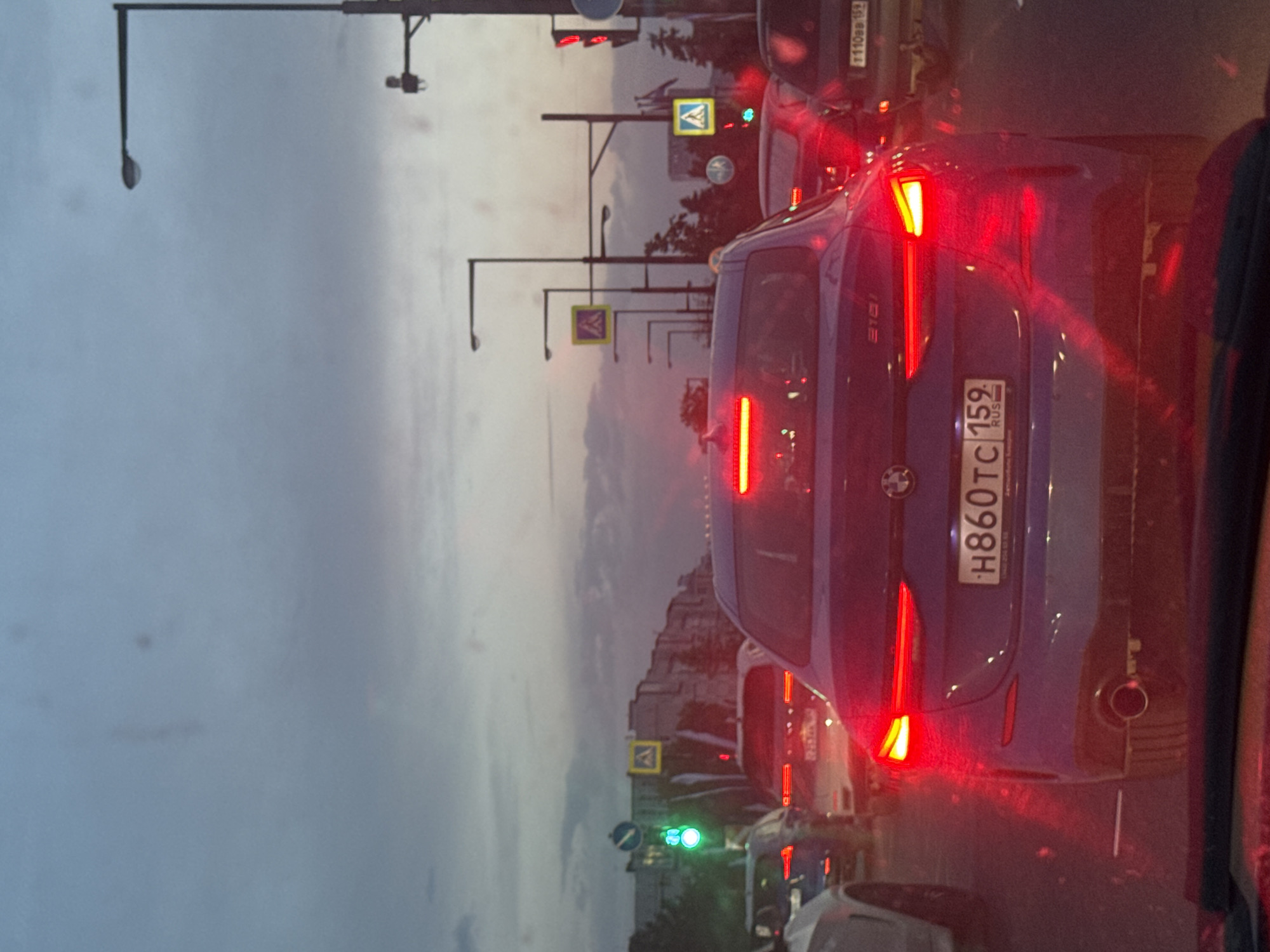 The image shows a traffic scene in Perm, Russia. A blue BMW with license plate number H860TC 159 is in a line of cars. Traffic lights are visible, showing a green light. There are pedestrian crossing signs. The sky is cloudy. Other cars are also present in the shot.