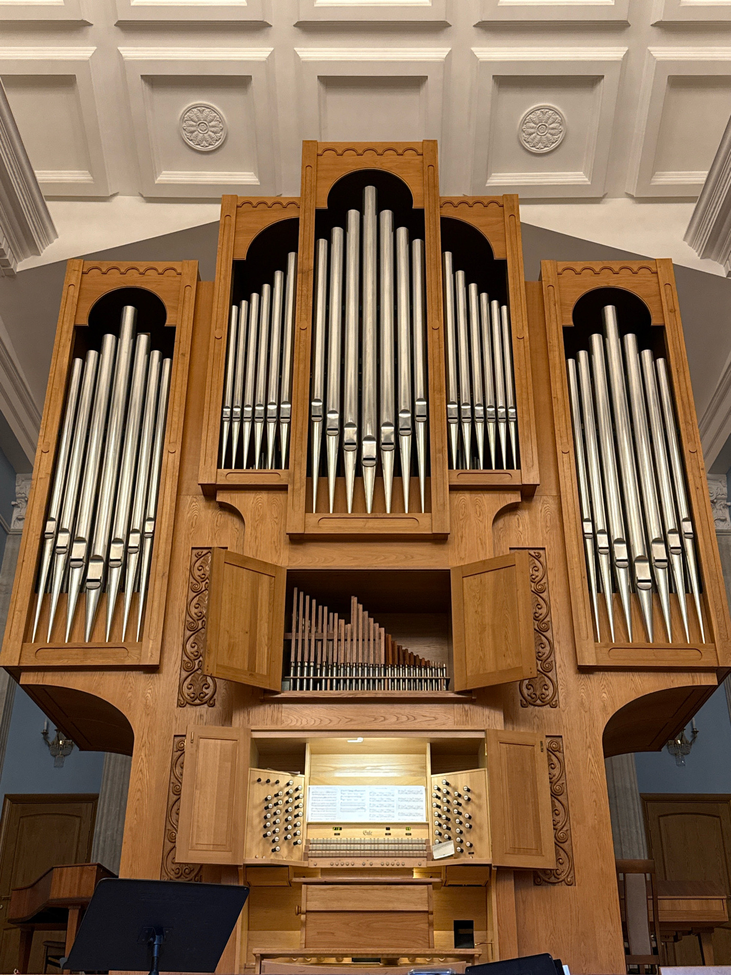 The image shows a large, ornate wooden pipe organ with silver pipes. The organ is located in what appears to be a large hall or church, with a decorative ceiling. The organ has multiple levels of pipes, as well as keyboards and stops. There are also decorative carvings on the wooden casing of the organ. The lighting suggests it is daytime, and the overall impression is one of grandeur and craftsmanship. There are no people visible in the image. The image does not provide any information about the city of Chelyabinsk, Russia.