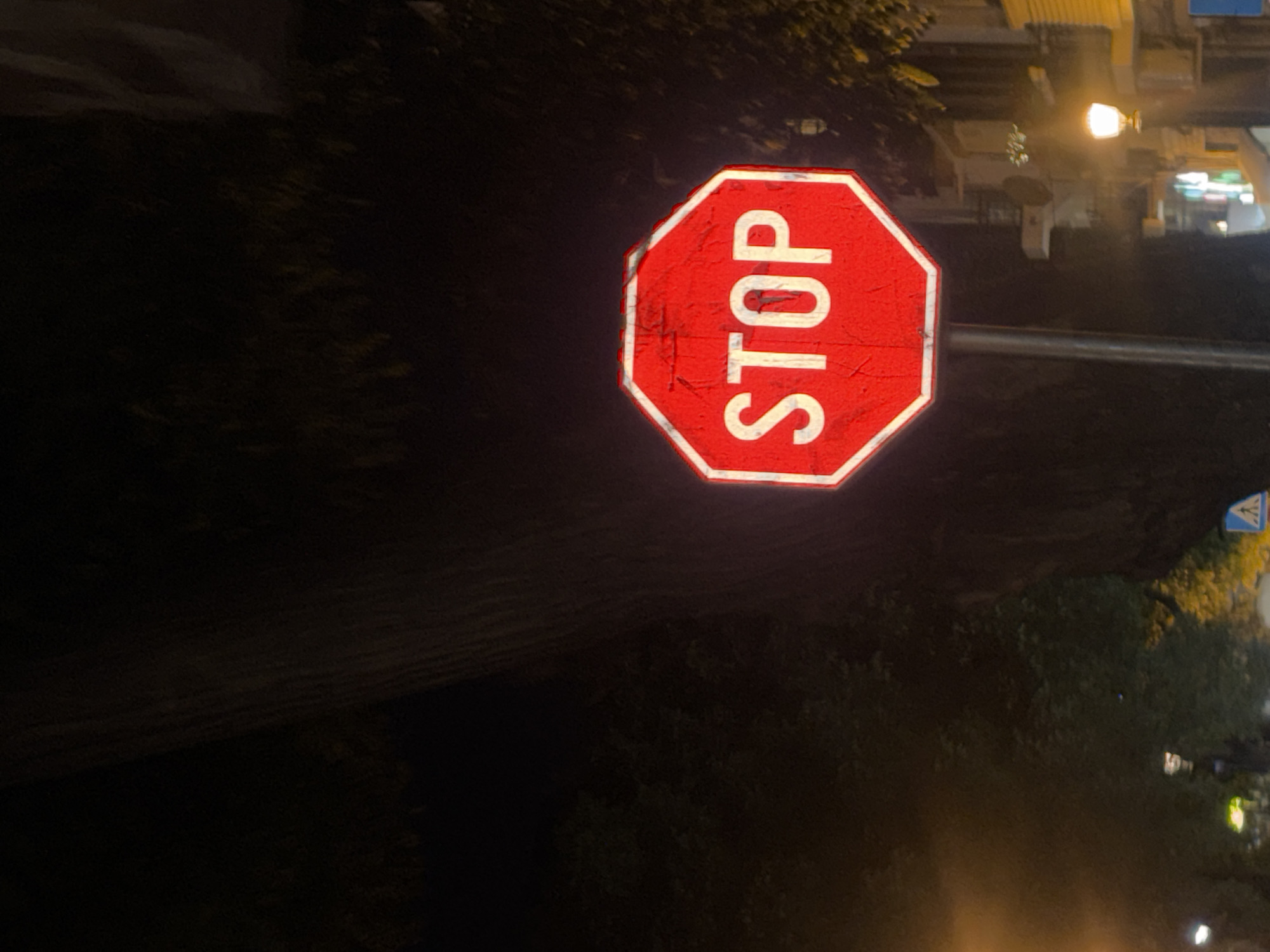 A red, octagonal stop sign with white lettering that reads "STOP" is illuminated by streetlights at night. The sign is mounted on a metal pole. In the background, there are trees, buildings, and streetlights, suggesting an urban environment. There are no people visible in the image. The scene is located on a street in the city of Plovdiv, Bulgaria.