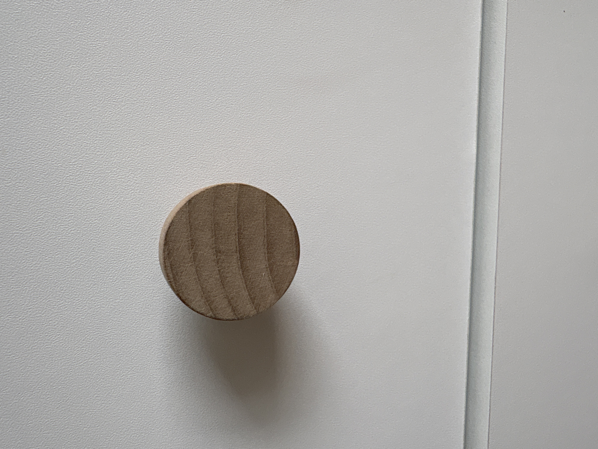 The image shows a close-up of a round, light-brown wooden knob attached to a white, textured surface. To the right of the knob is a vertical line suggesting the edge of a door or panel. There are no people visible. The location in the city of Ембаево, Russia, is not verifiable from the image.