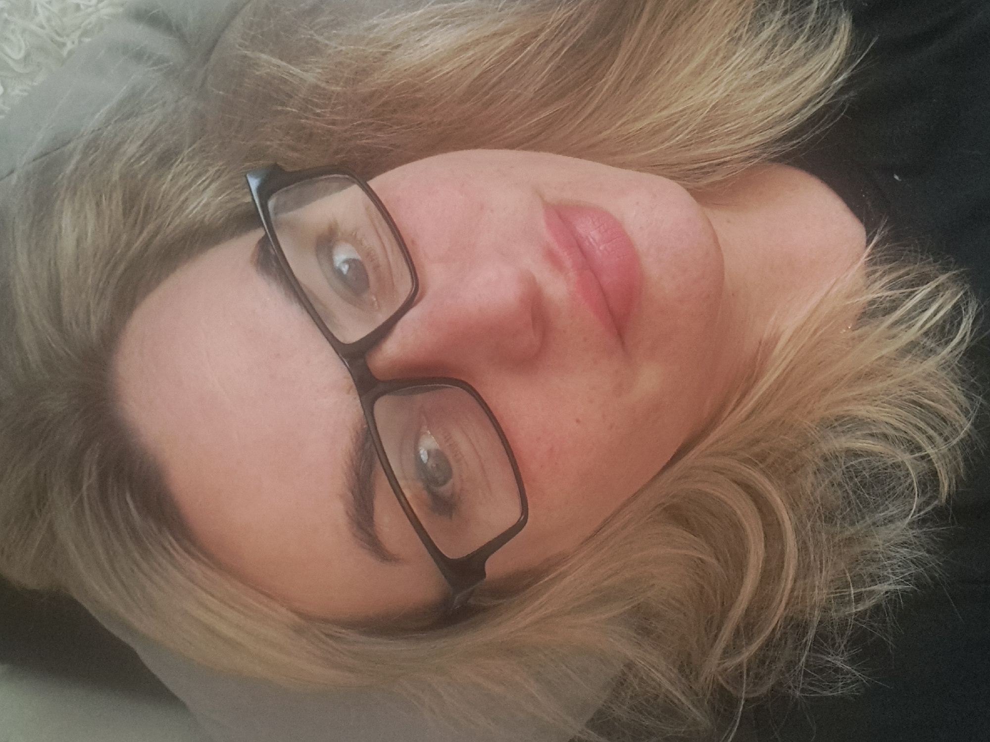 A fair-skinned woman with blonde hair and glasses is lying on a soft surface. The subject appears to be indoors. Location in Elektrostal, Russia is unknown.