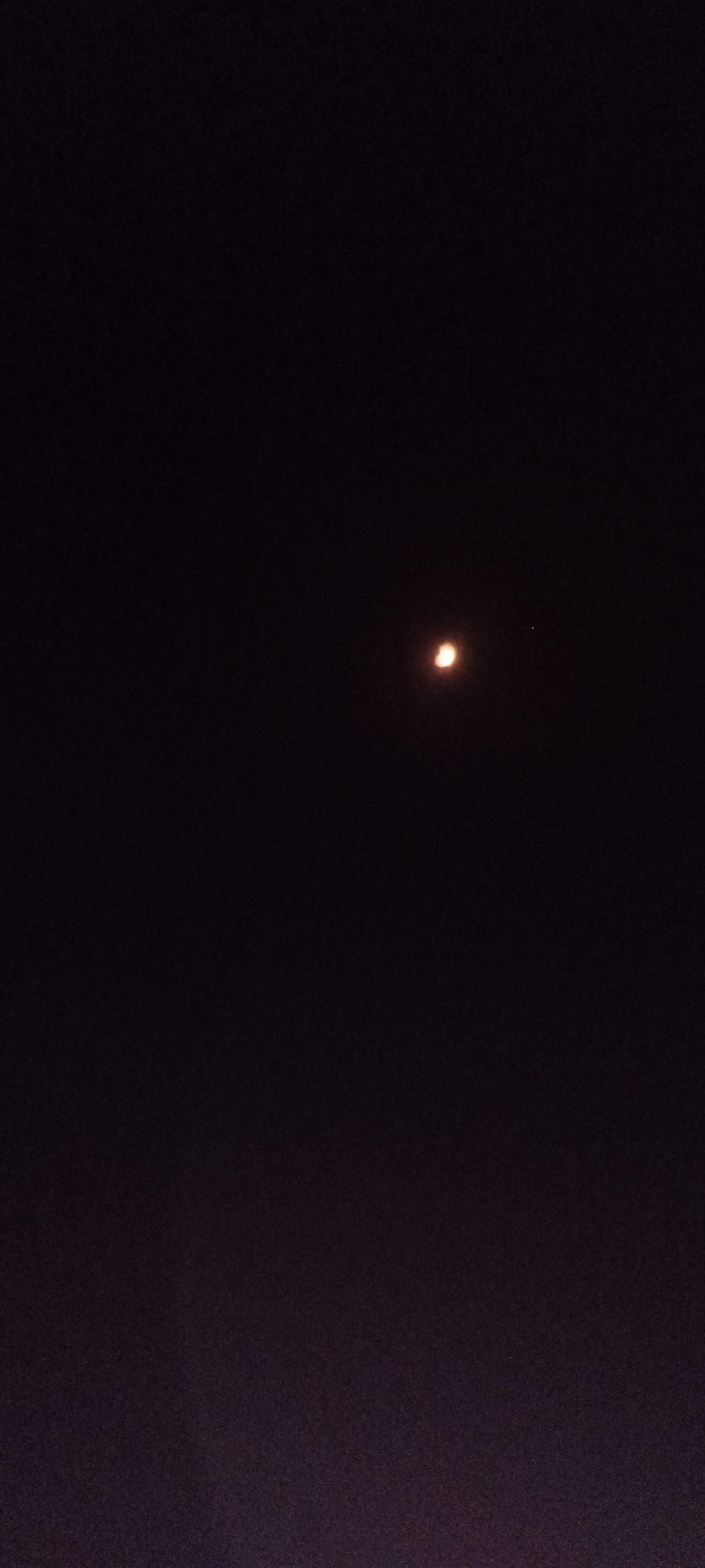 The image shows a dark night sky with a small, bright celestial body, likely the moon, appearing as a crescent shape with a reddish-orange hue. To the right of this celestial body, there is a much smaller, fainter, white point of light, which could be a star or another planet. The background is predominantly black, indicating nighttime. The image does not contain any elements that can be used to determine its location in Adai, Spain.
