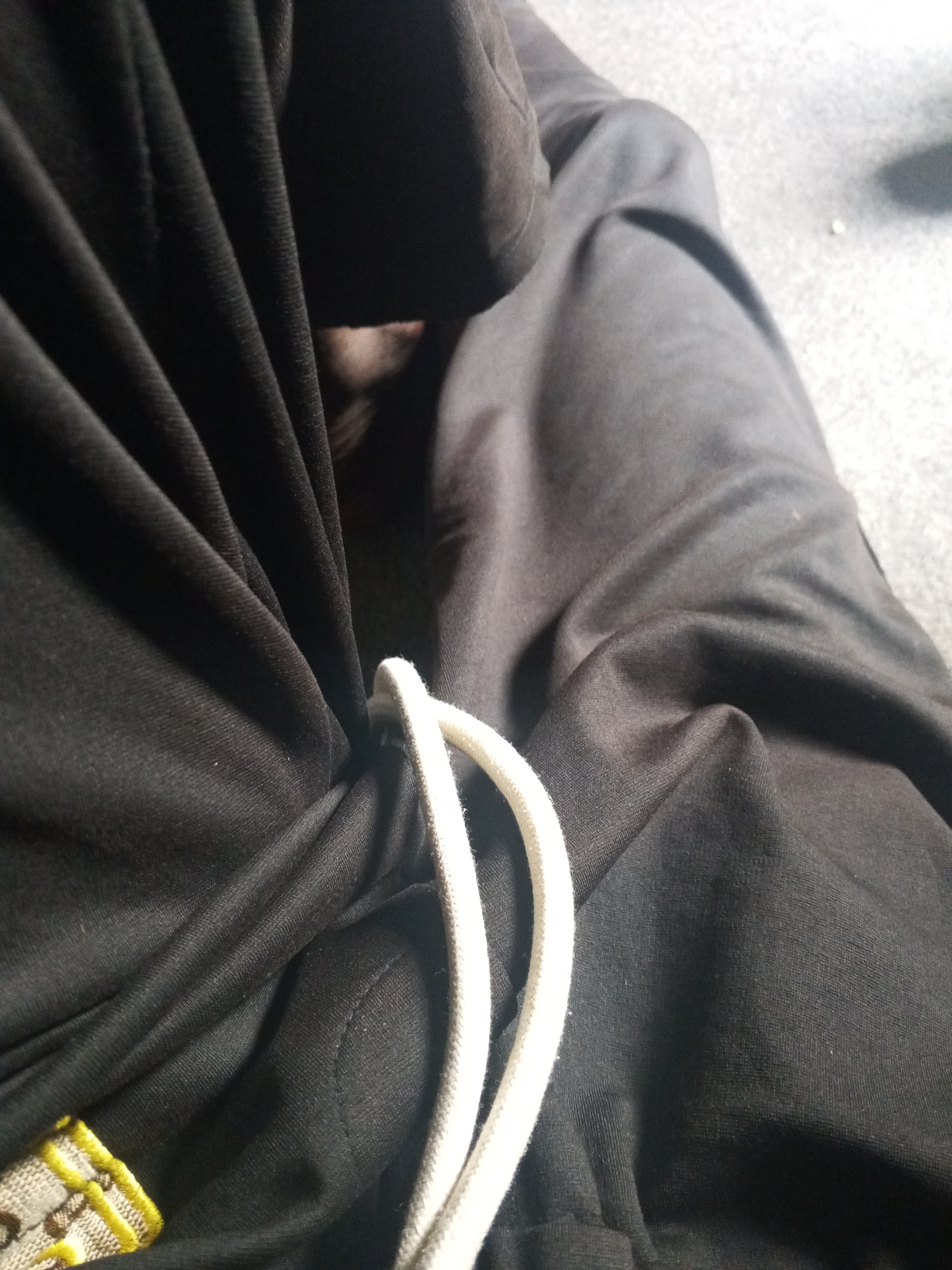 A person wearing black sweatpants with a white drawstring is sitting on a gray surface. The location is not discernible from the image.