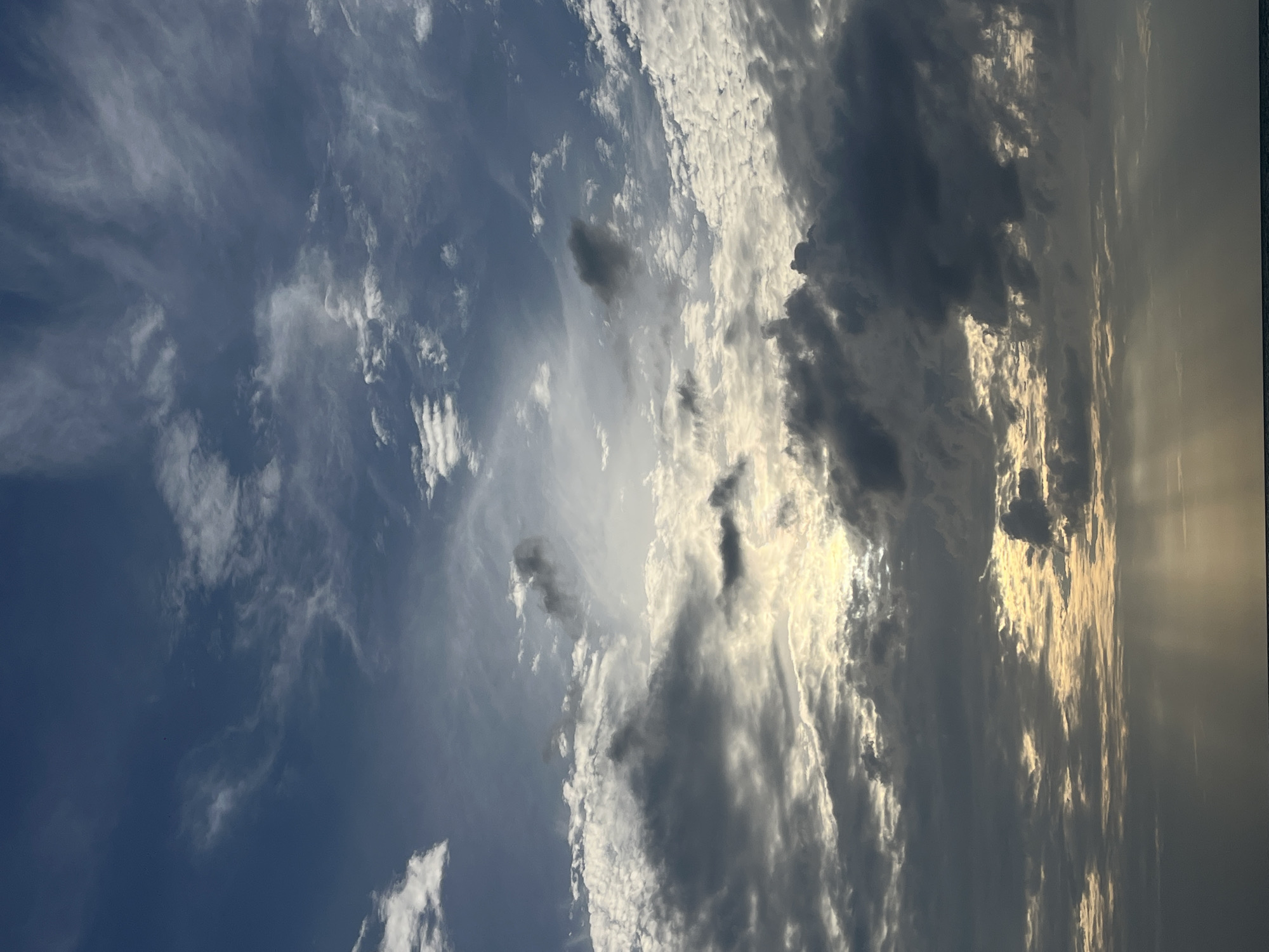 The image depicts a dramatic sky with a mix of dark and light clouds, suggesting either sunrise or sunset over the ocean. Rays of sunlight pierce through gaps in the clouds, illuminating parts of the sky and the water's surface. The lower portion of the image shows a thin strip of dark water, likely the sea, with a faint horizon line. There are no people, buildings, or specific landmarks visible, making it difficult to pinpoint an exact location within Ko Samui District, Thailand, beyond the general setting of a coastal environment. The scene is entirely focused on the atmospheric conditions of the sky and sea.