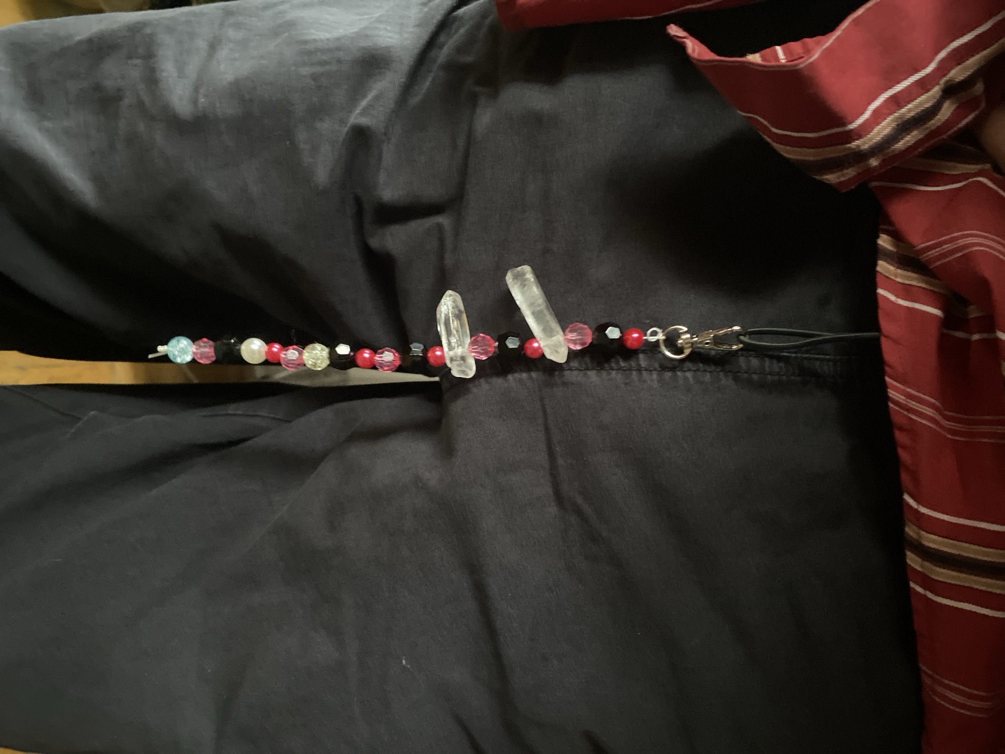 The image shows a person wearing dark pants and a red and white striped shirt. Resting on the pants is a lanyard decorated with various beads in colors like red, pink, black, and clear, as well as two clear quartz crystals. The lanyard has a silver clip attached. The location cannot be determined based on the provided image alone. There is no information suggesting a location in Moscow, Russia.